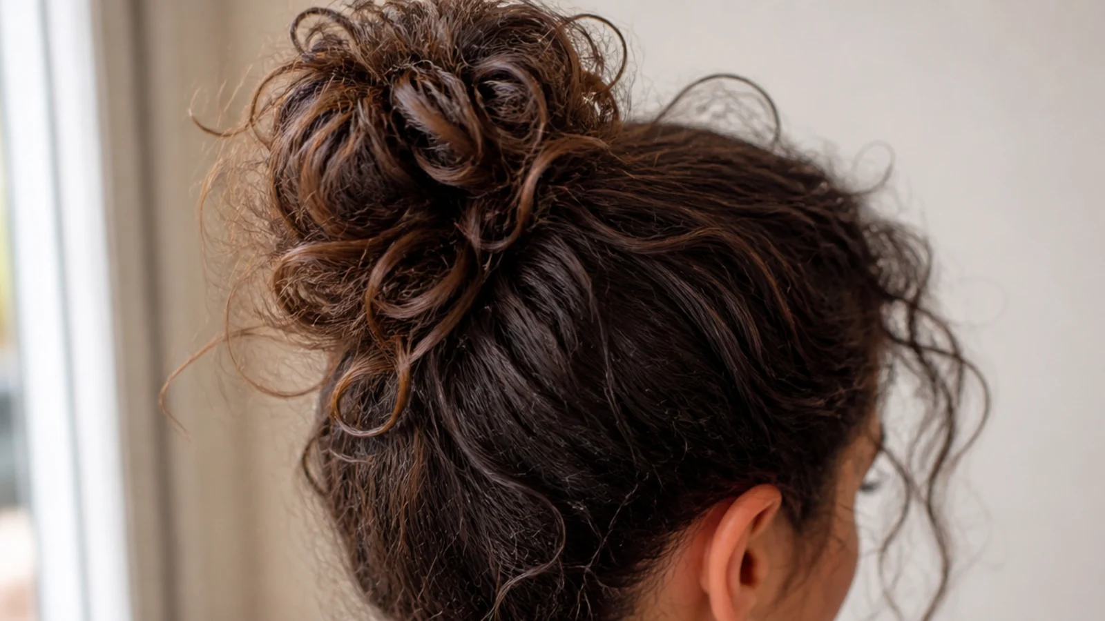 High bun on frizzy curly hair with escaped wisps around the temples and nape