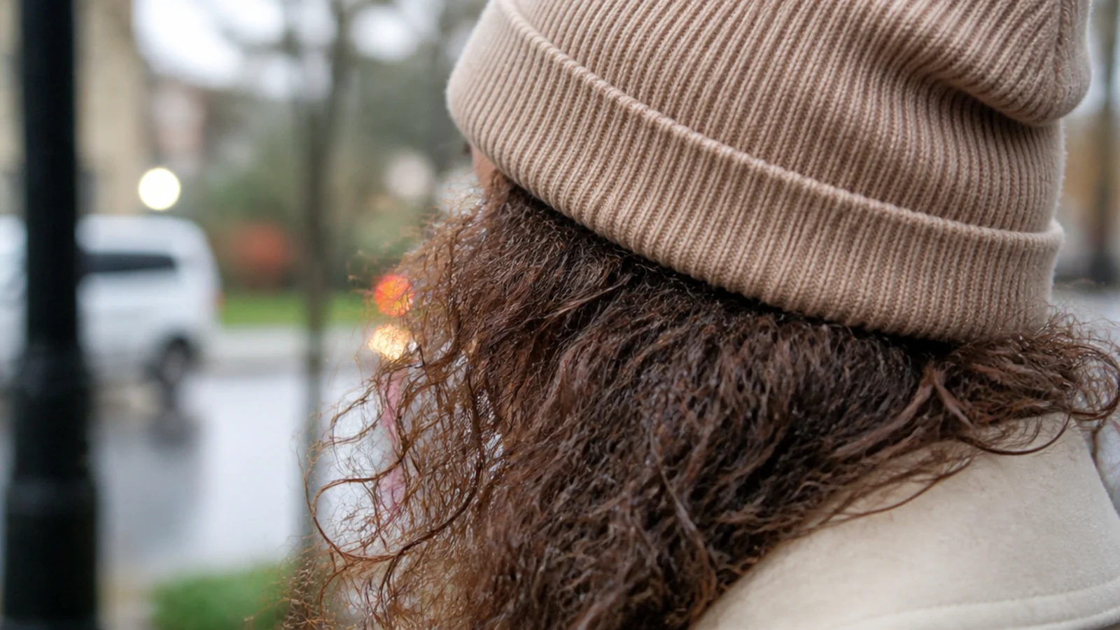 Frizzy curly hair spilling out from under a ribbed beanie on a rainy day with a damp halo