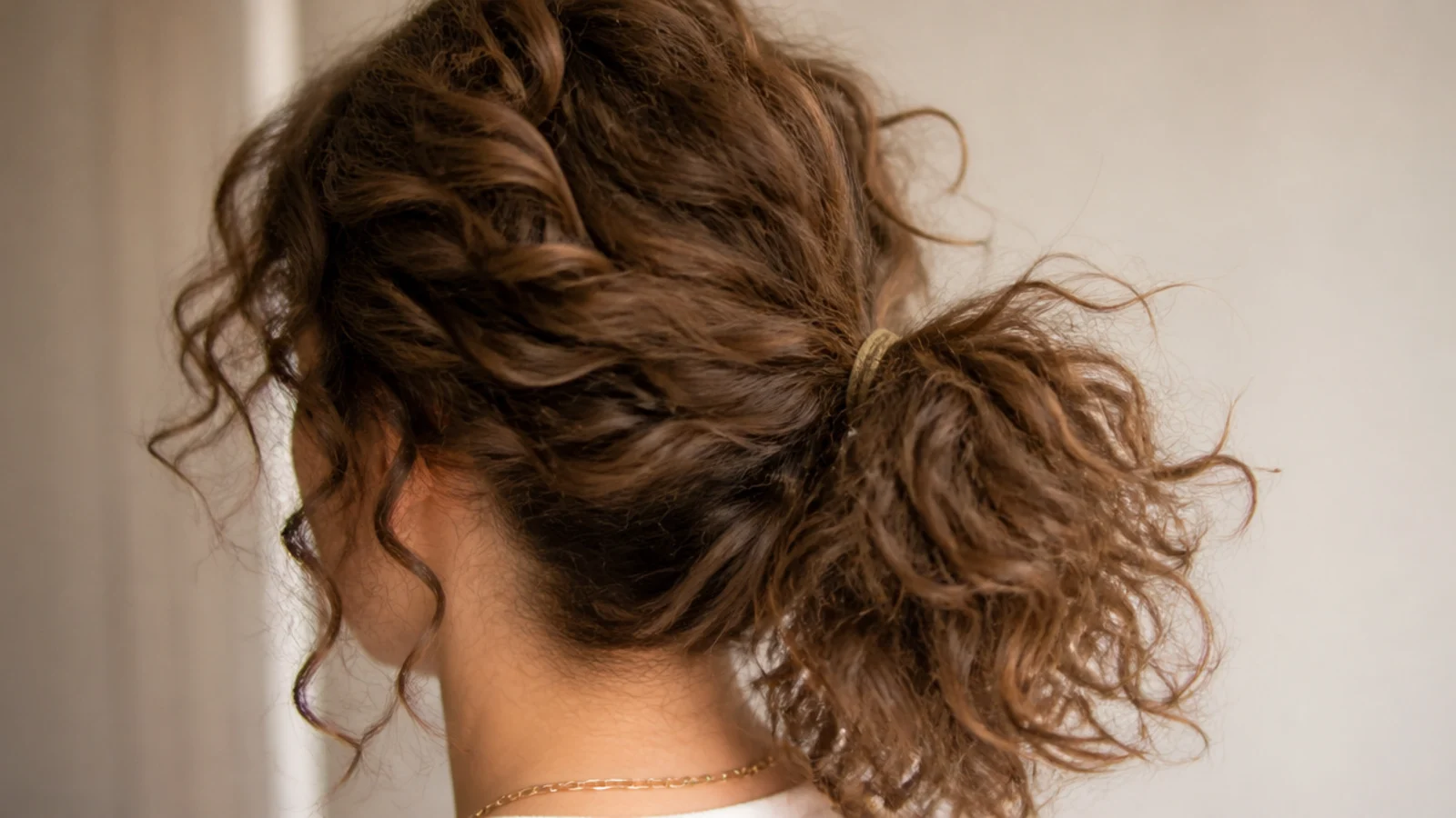 Mid height frizzy curly ponytail with a soft cloud of crown volume above a loose elastic