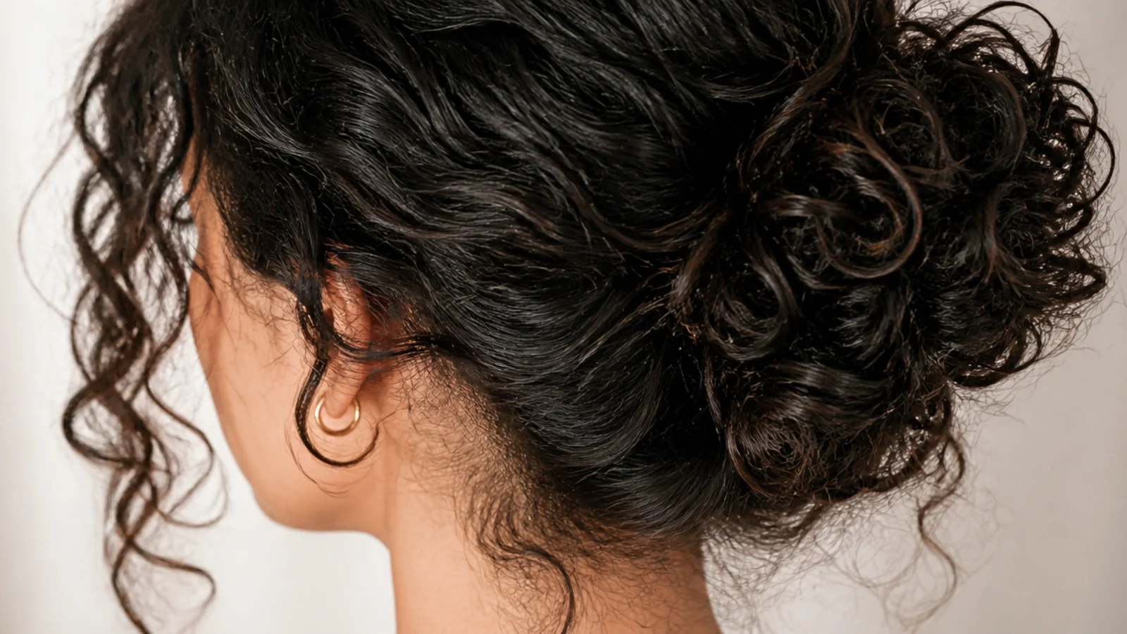 Half up curly bun with loose face framing curls and soft frizz left visible around the hairline