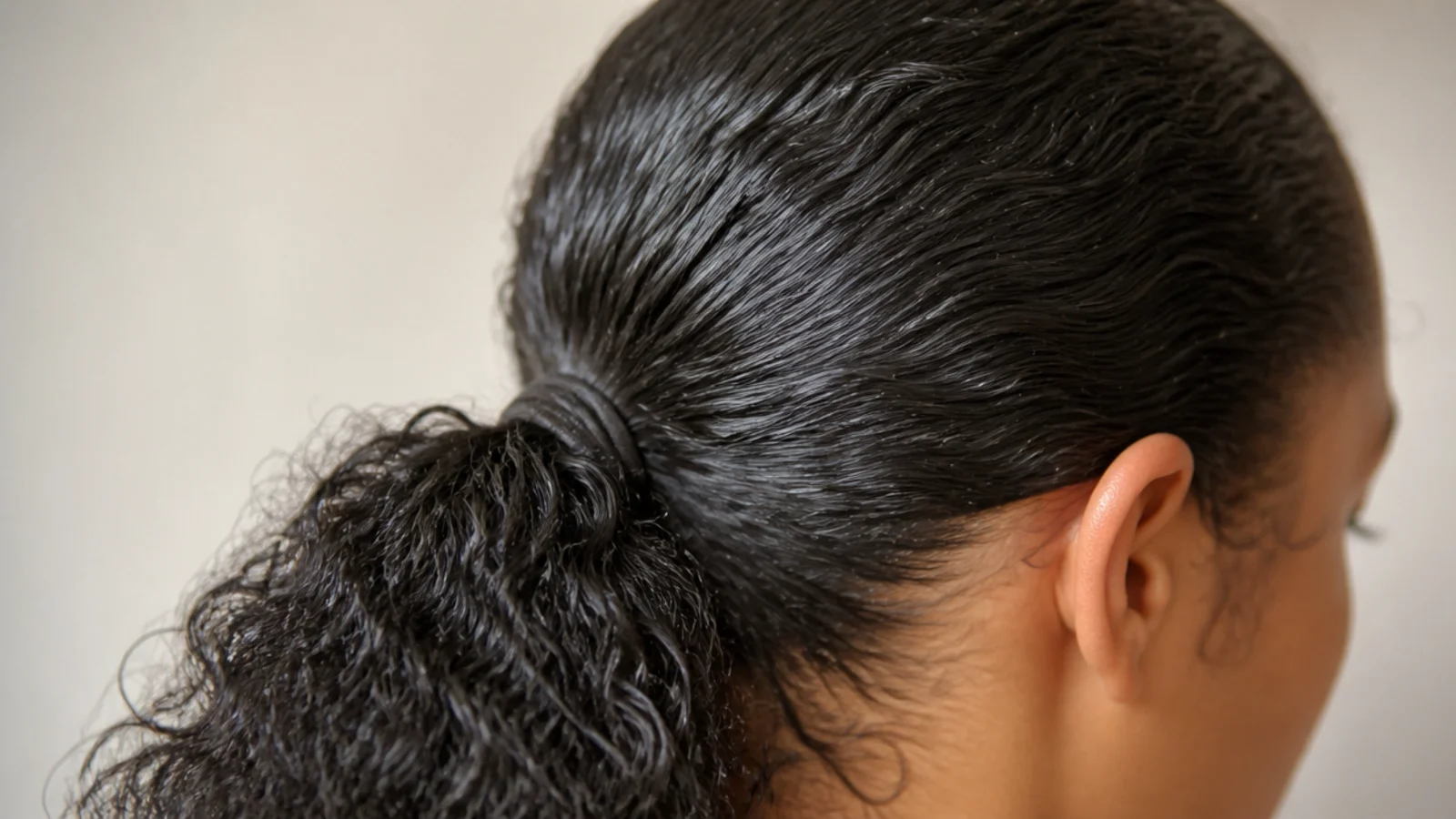 Slicked back low ponytail on frizzy hair with a wet look finish and a smooth crown