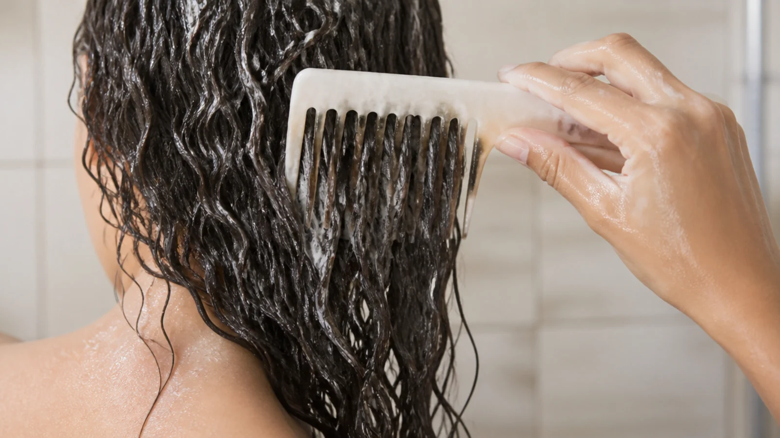 Wide tooth comb detangling conditioner coated frizzy hair in the shower without breakage