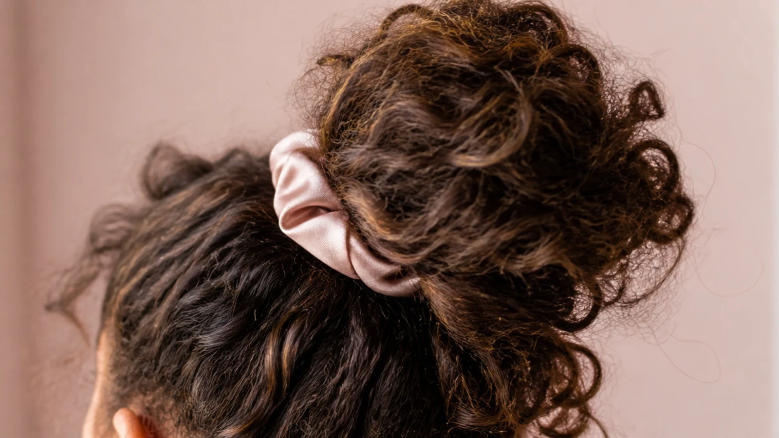 Curly frizzy hair gathered into a loose high pineapple with a satin scrunchie for overnight