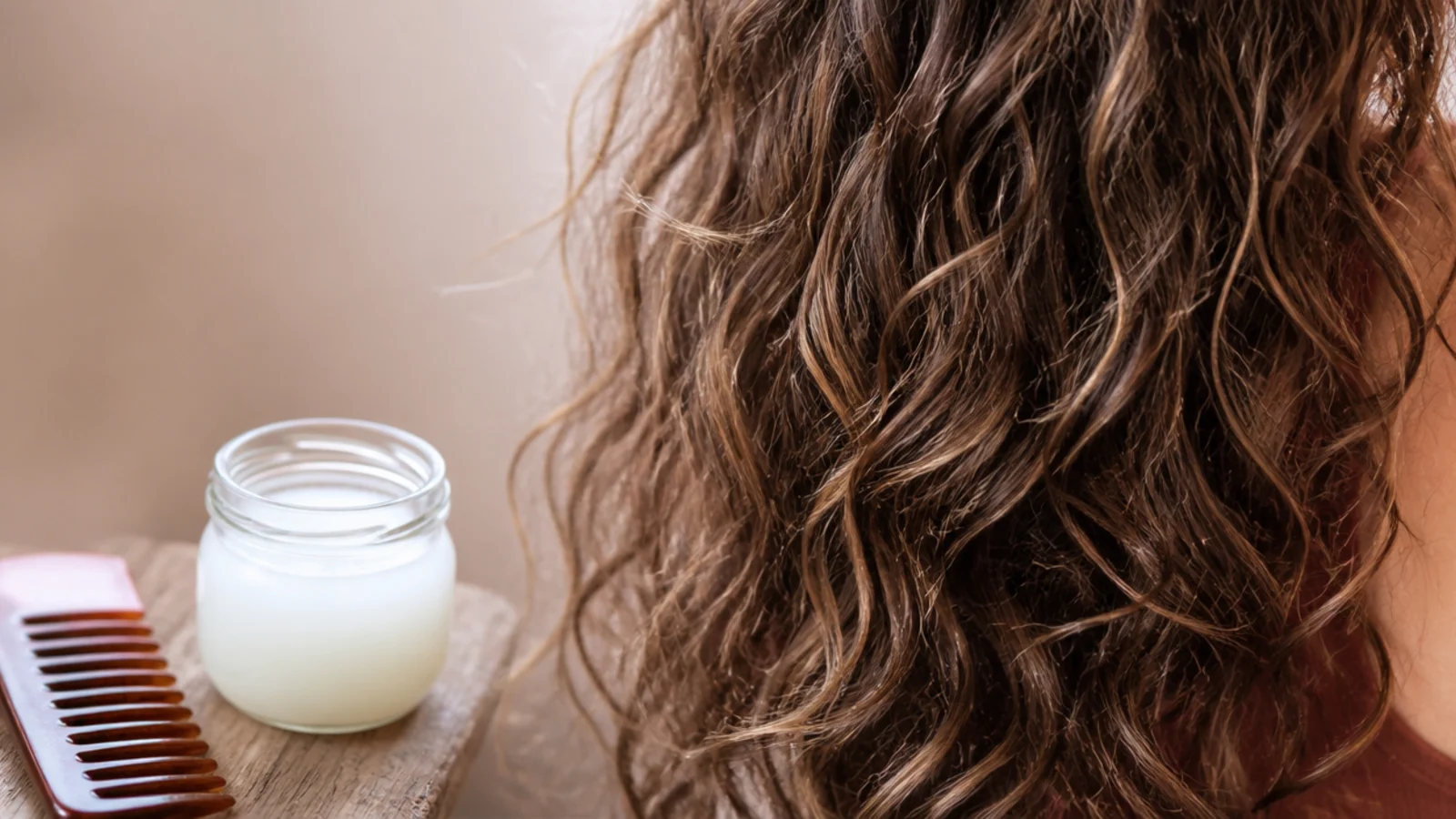 Coconut oil pre-shampoo treatment melted in a jar next to a wide-tooth comb for frizzy hair