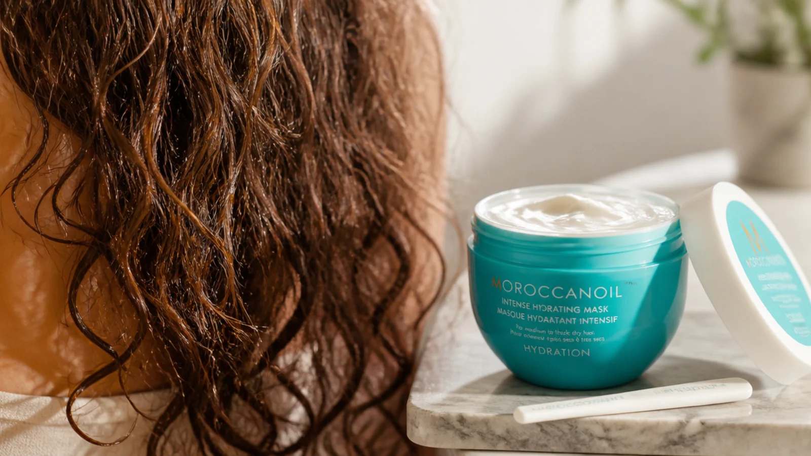 Moroccanoil Intense Hydrating Mask jar with a spatula beside damp frizzy hair