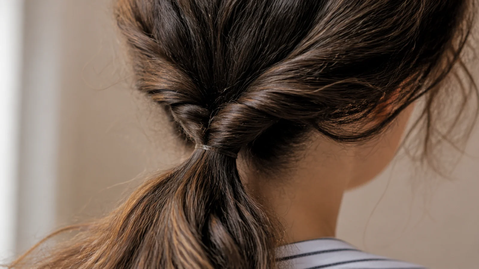 Two-strand rope twist low ponytail on medium length frizzy hair secured with two clear elastics