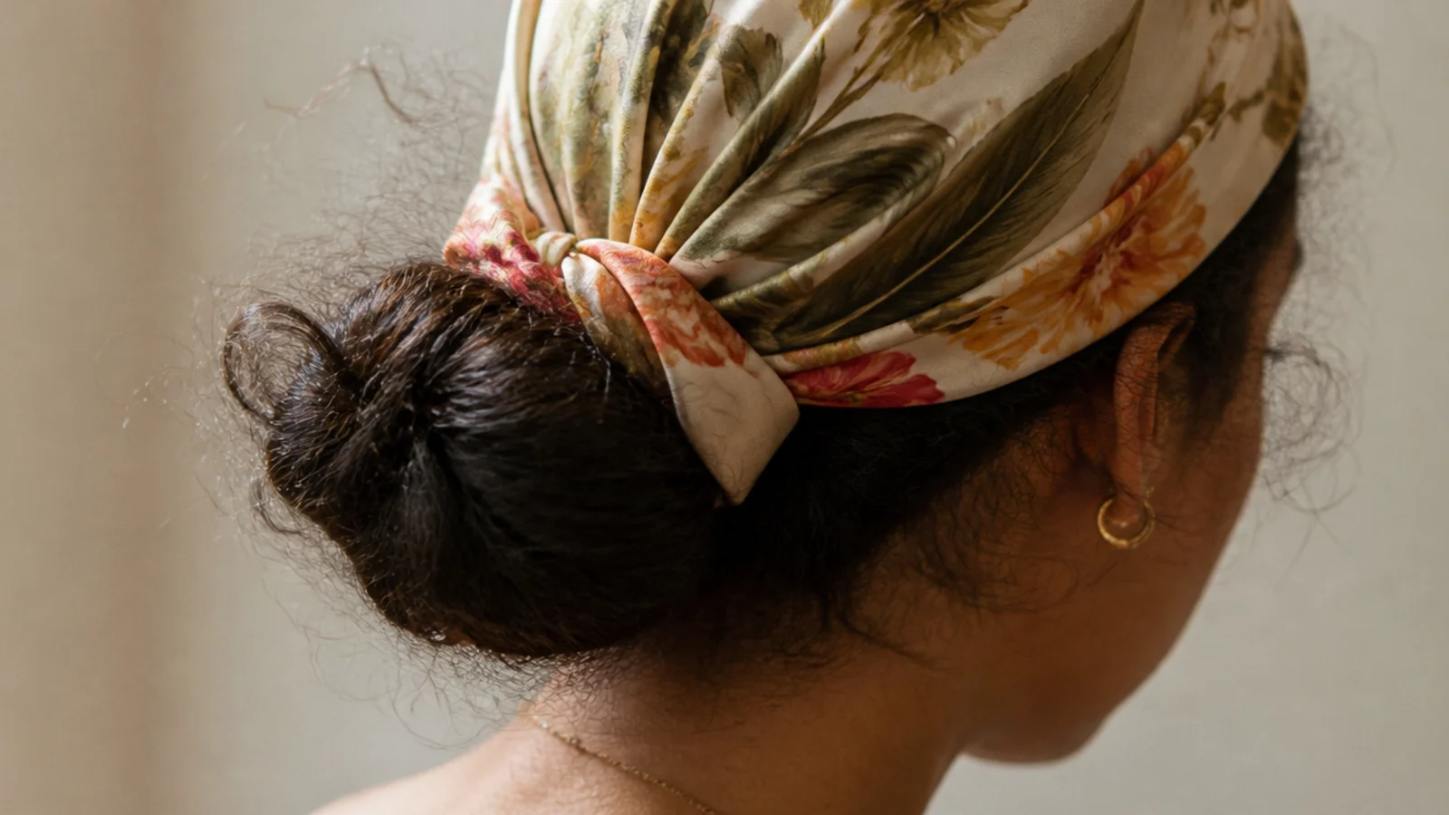 Silk scarf tied as a headwrap over frizzy hair with a low bun showing beneath the knot
