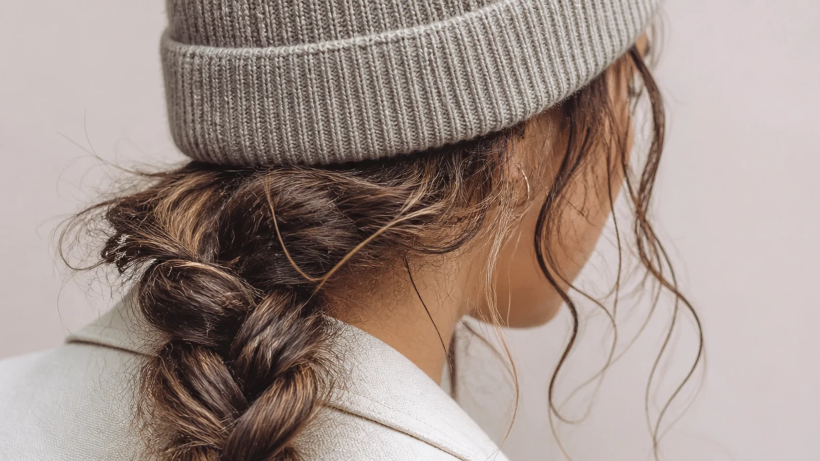 Low side braid worn under a ribbed beanie on frizzy hair for a rainy day with soft face-framing pieces