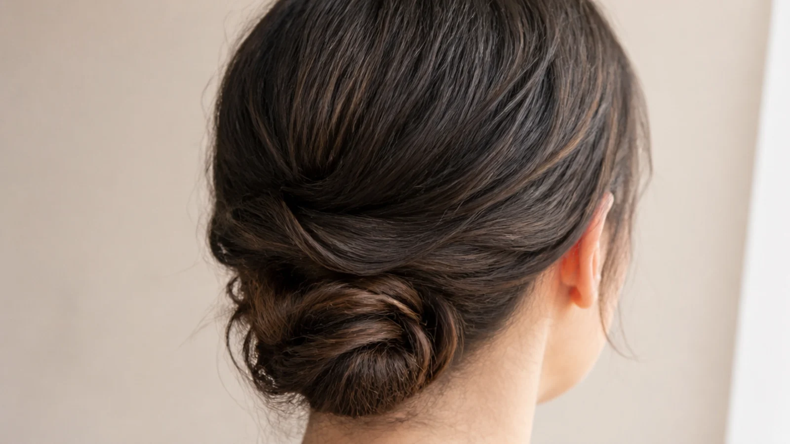 Sleek middle-part low chignon on fine frizzy hair rolled and pinned at the nape with a smooth crown