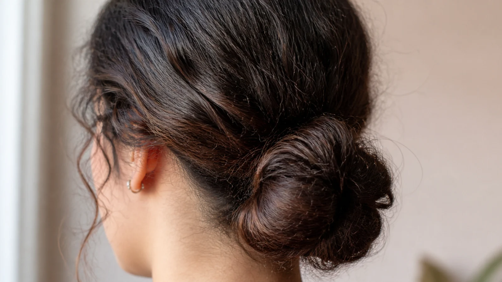 Low chignon at the nape on puffy frizzy hair with softly gathered sides rather than slicked back