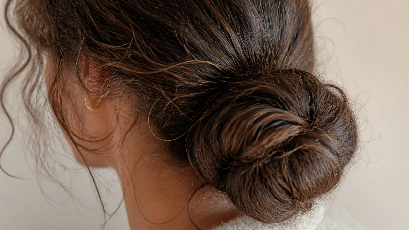 Low rolled bun on puffy frizzy hair created by tucking a loose ponytail up through its own base