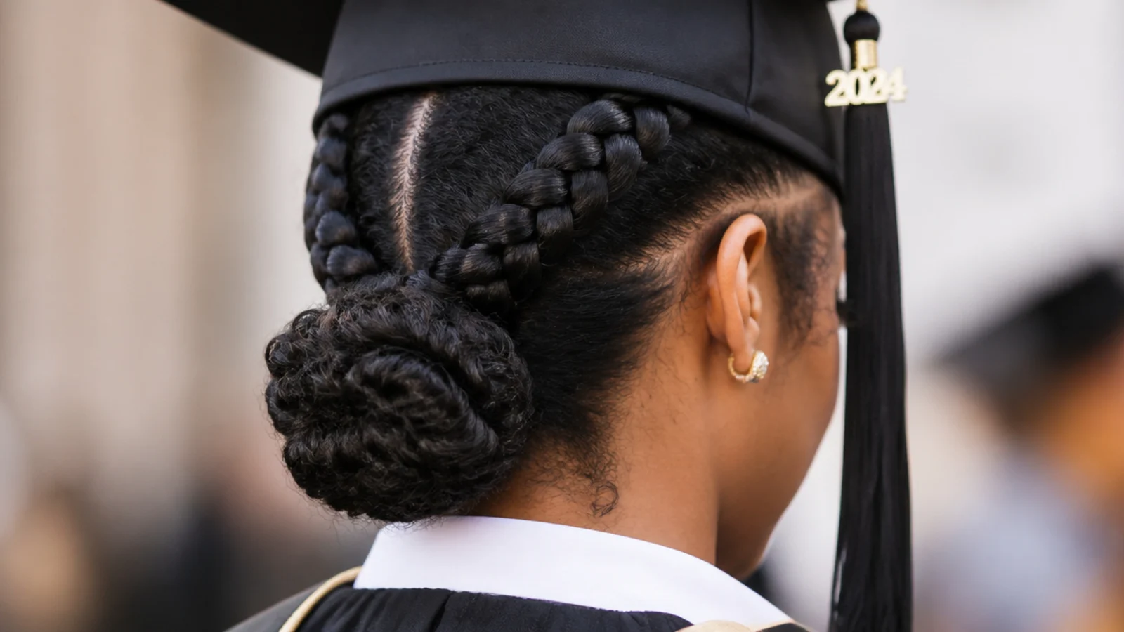Two cornrows feeding into a low bun as a braided graduation hairstyle for natural hair under a cap