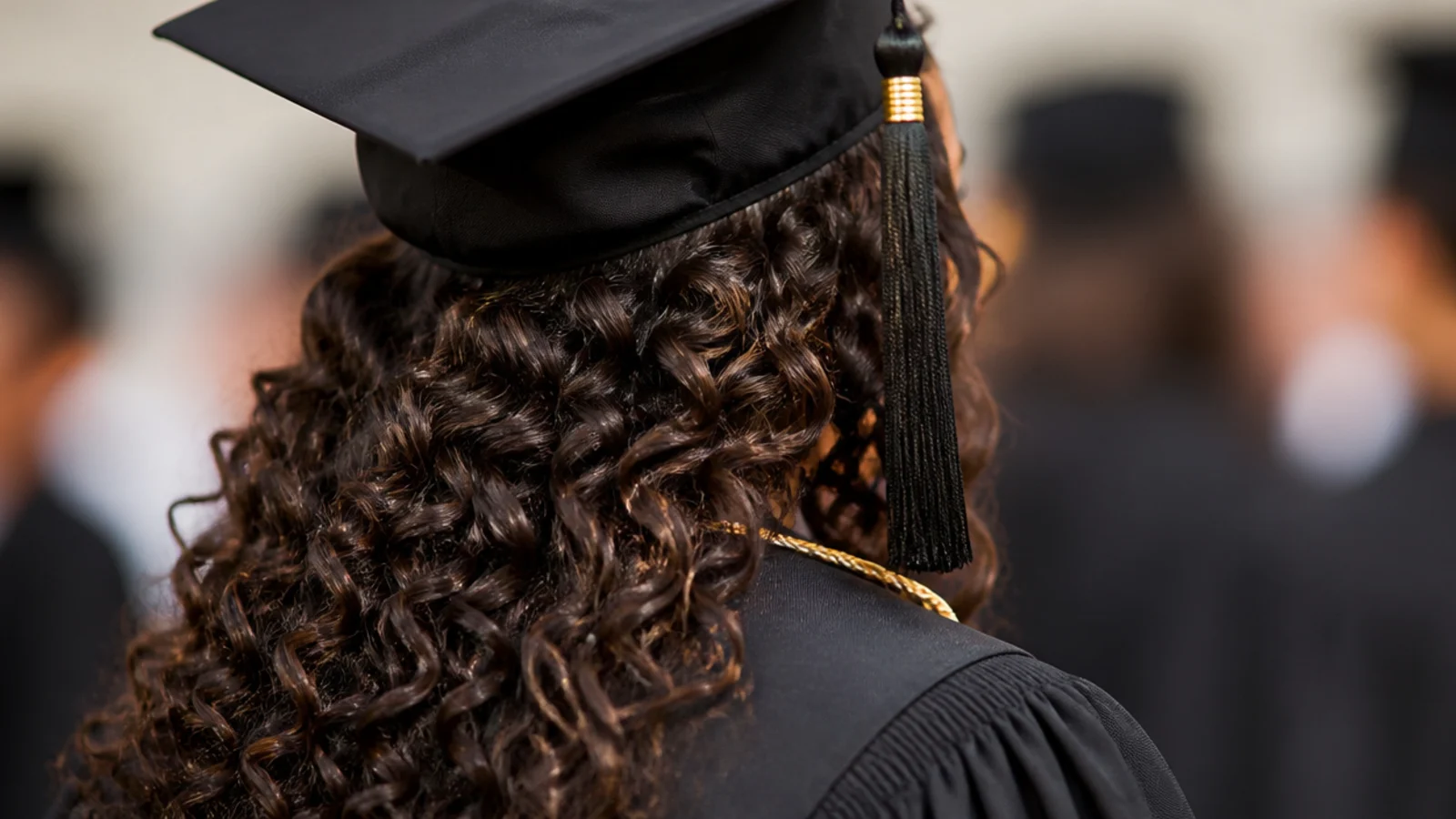 Side-swept 3A curly waves brought over one shoulder under a flat graduation cap
