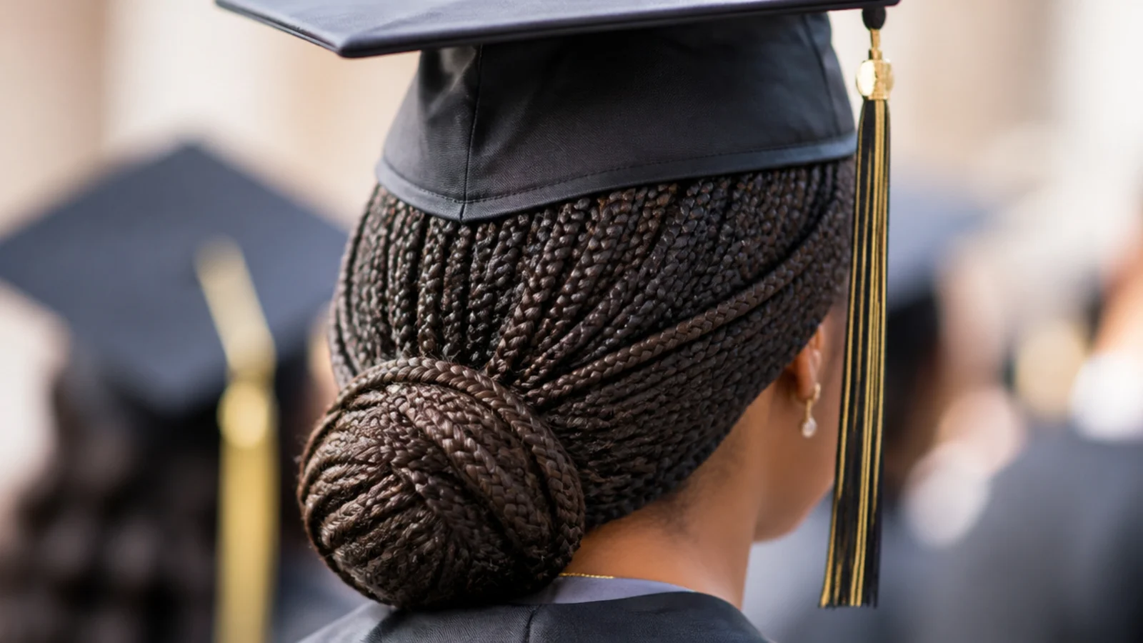 Mid-back knotless box braids gathered into a low bun at the nape under a graduation cap