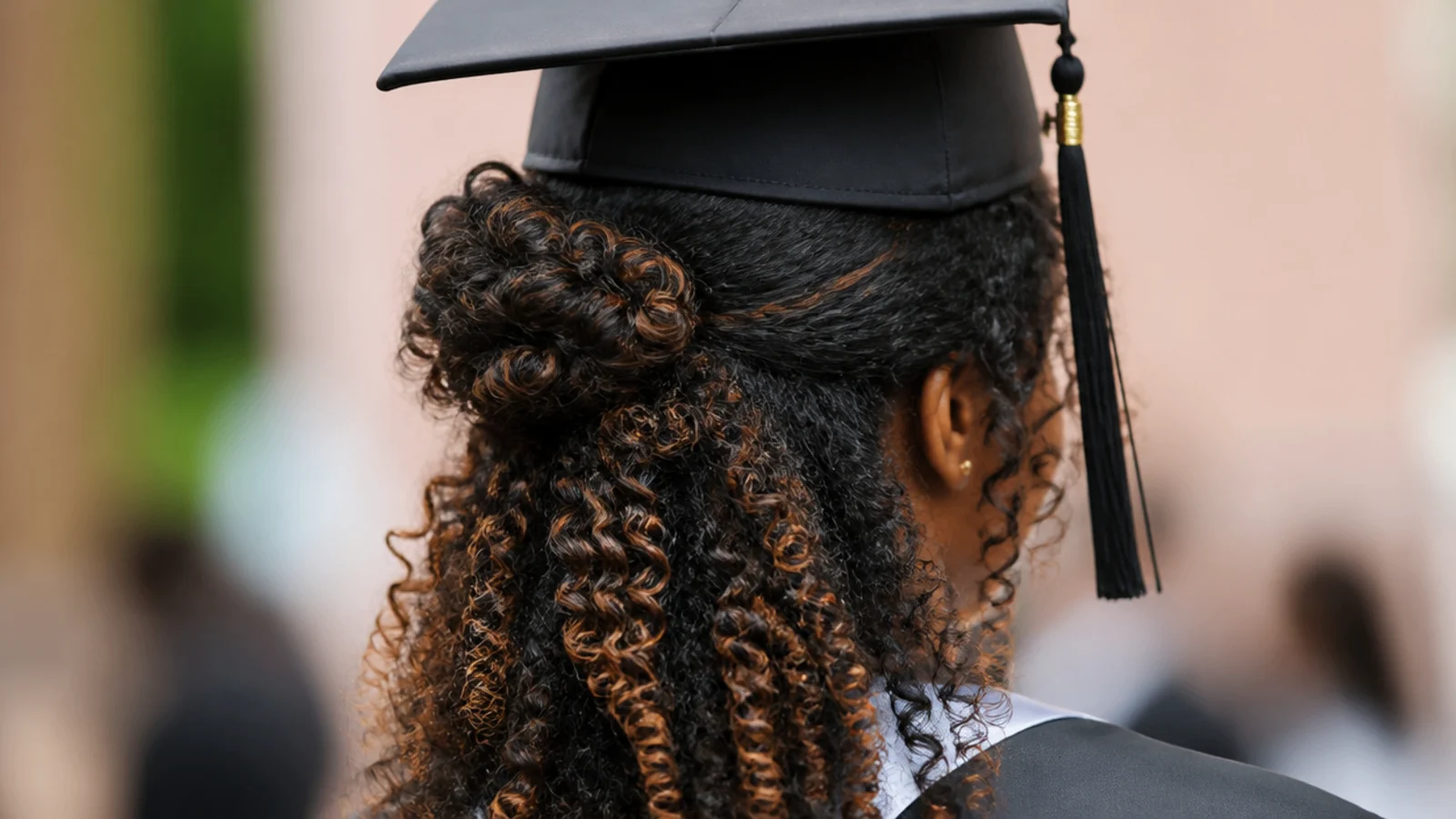 Half-up puff on natural hair with defined curls left loose below a graduation cap
