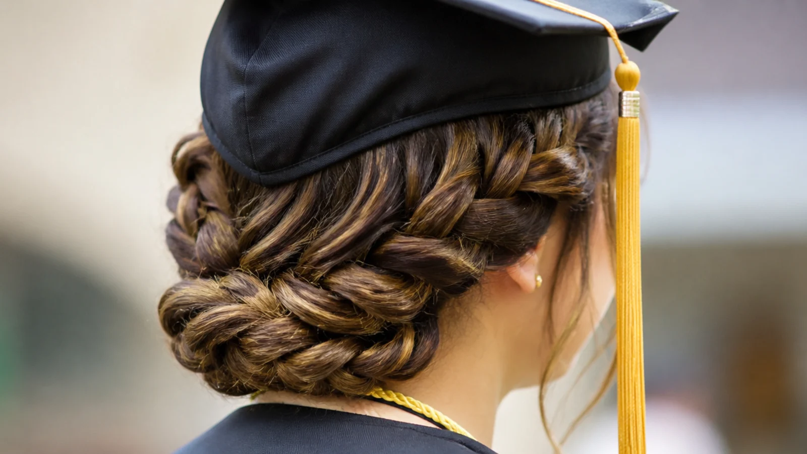Low braided halo graduation hairstyle pinned around the back of the head at ear level below the cap