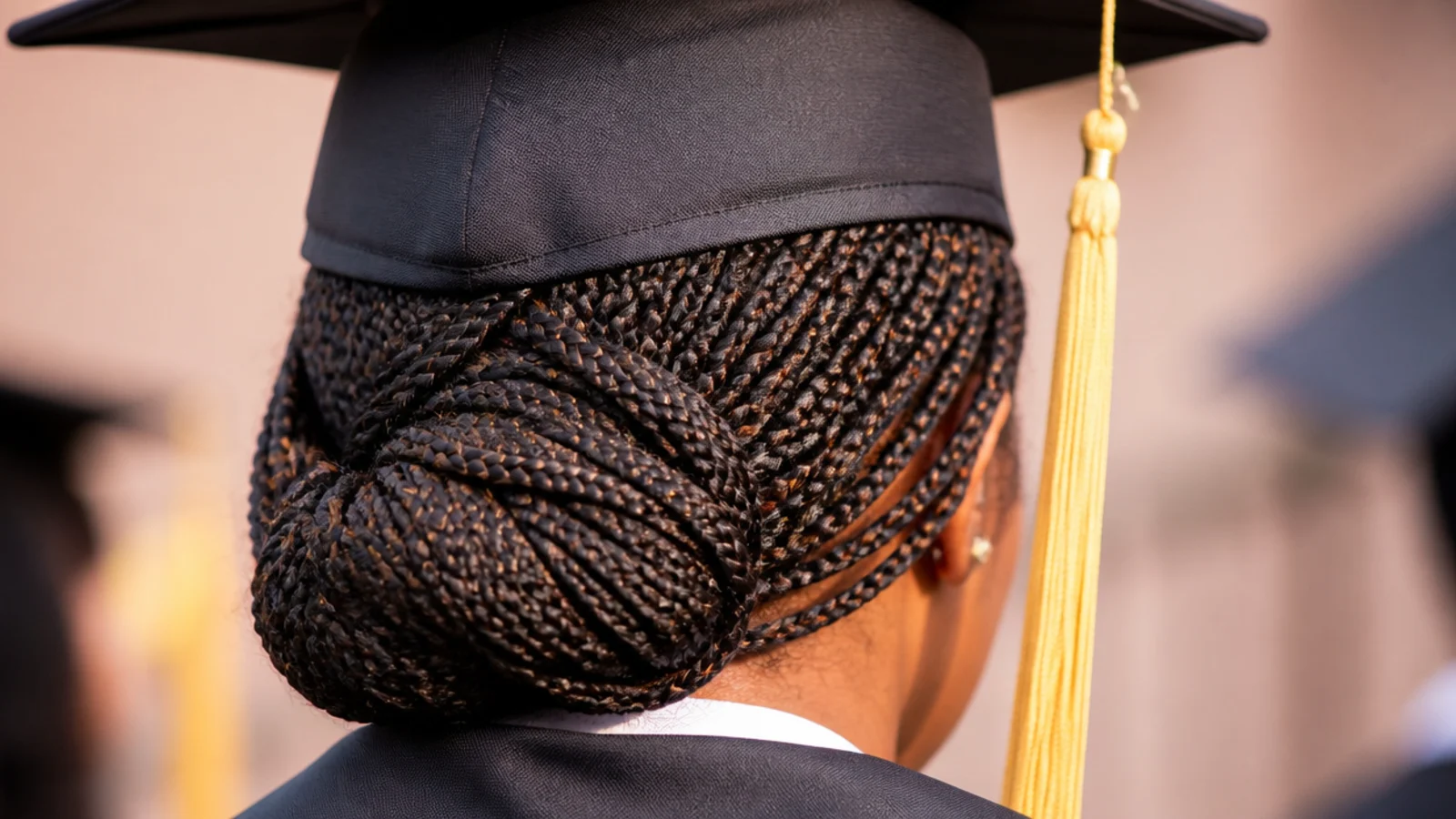 Knotless box braids gathered into a low bun at the nape under a graduation cap with gold tassel