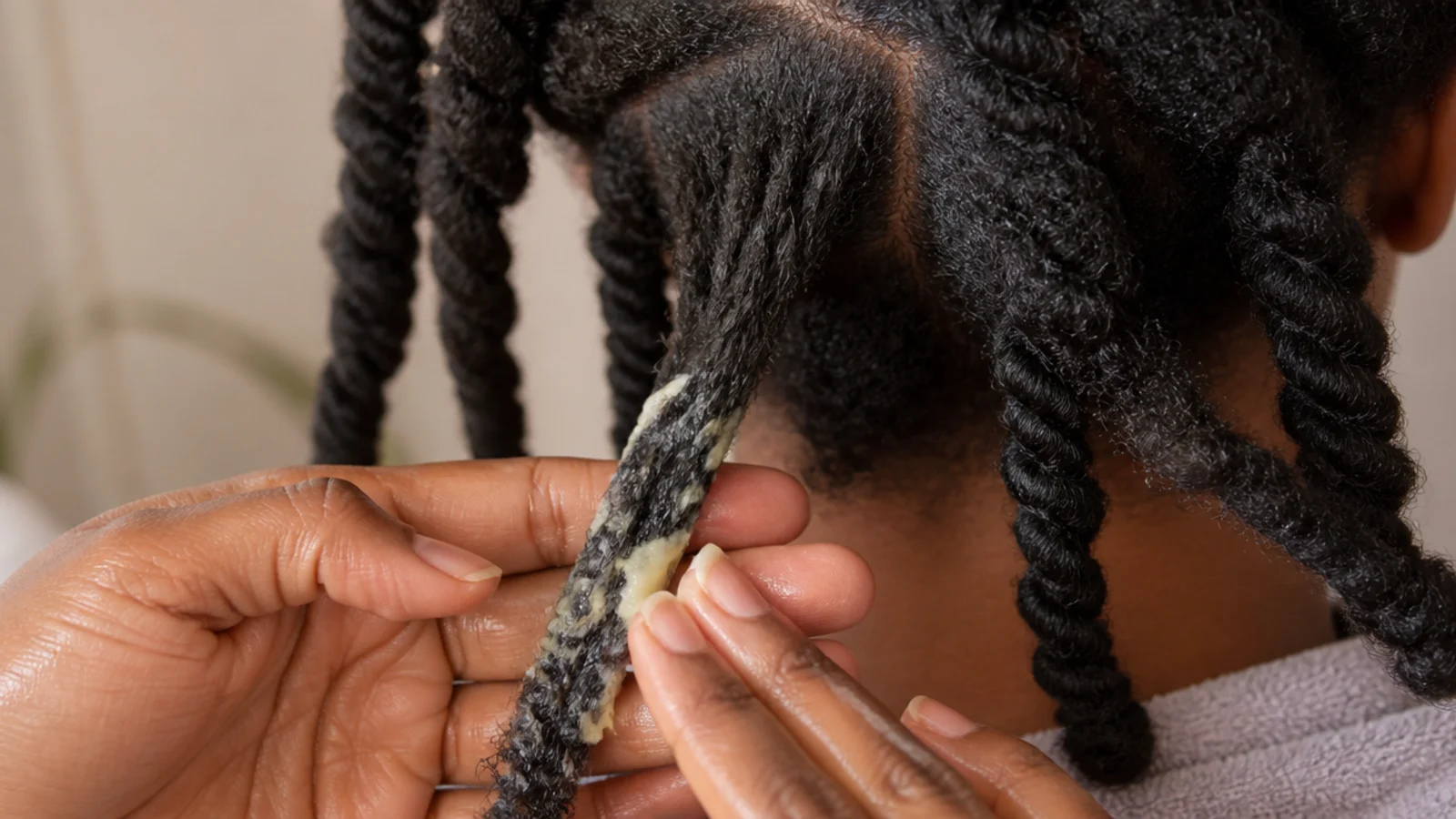 Shea butter being smoothed onto the ends of a stretched 4C two-strand twist