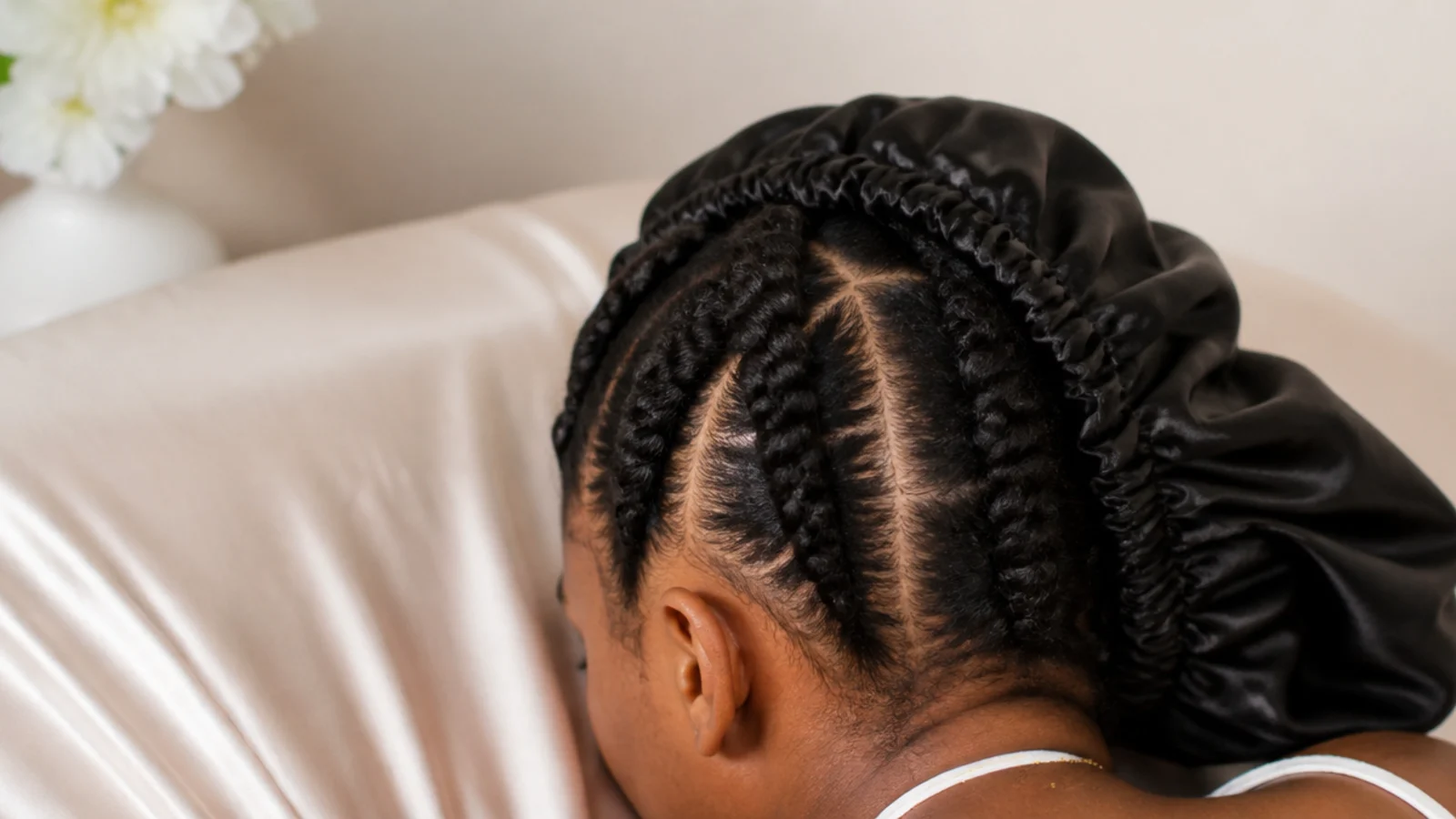 Black woman wearing a satin bonnet over twisted hair with a satin pillowcase on the bed