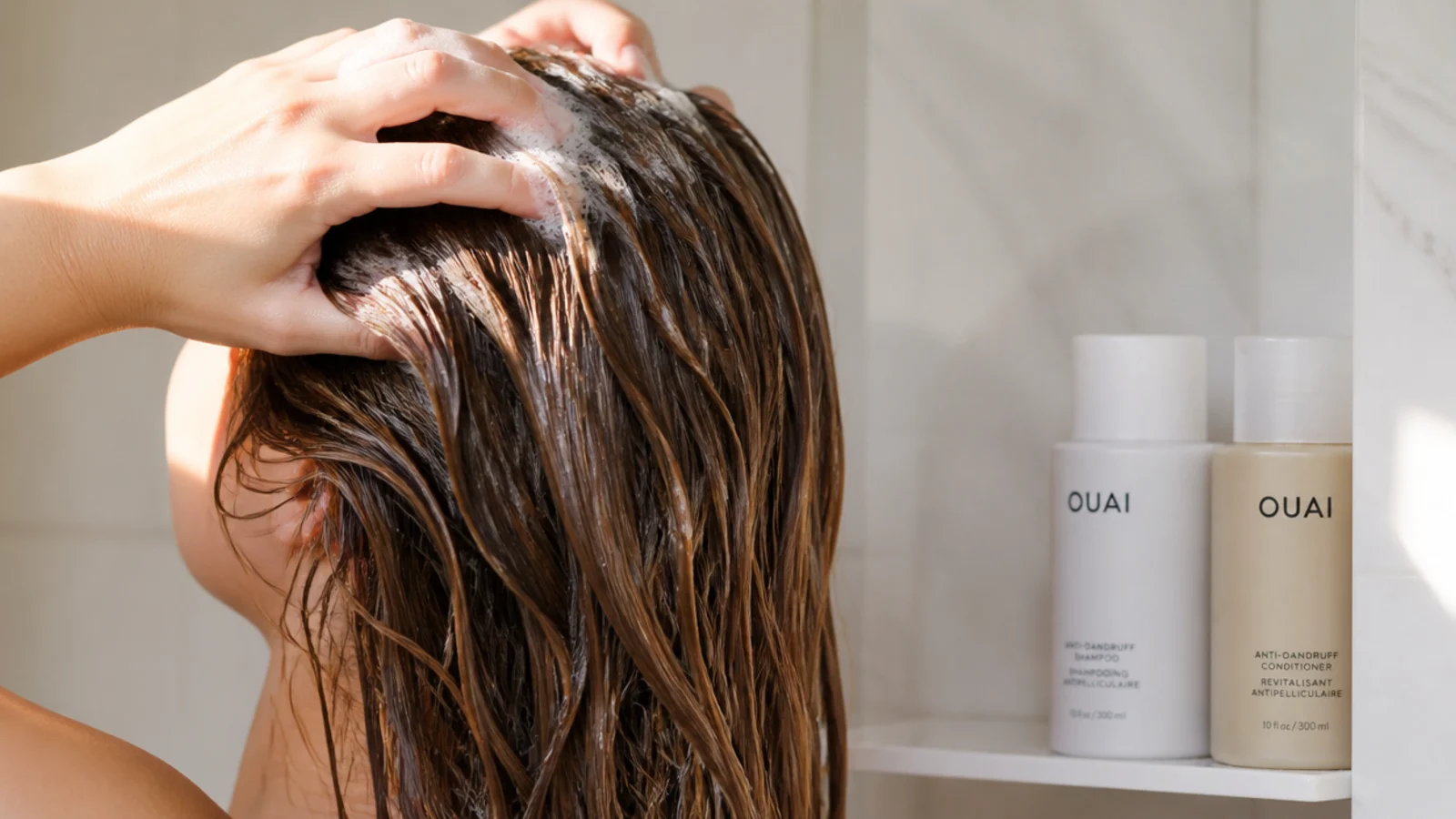 Shampoo and conditioner bottles in a shower with long hair being washed at the roots only