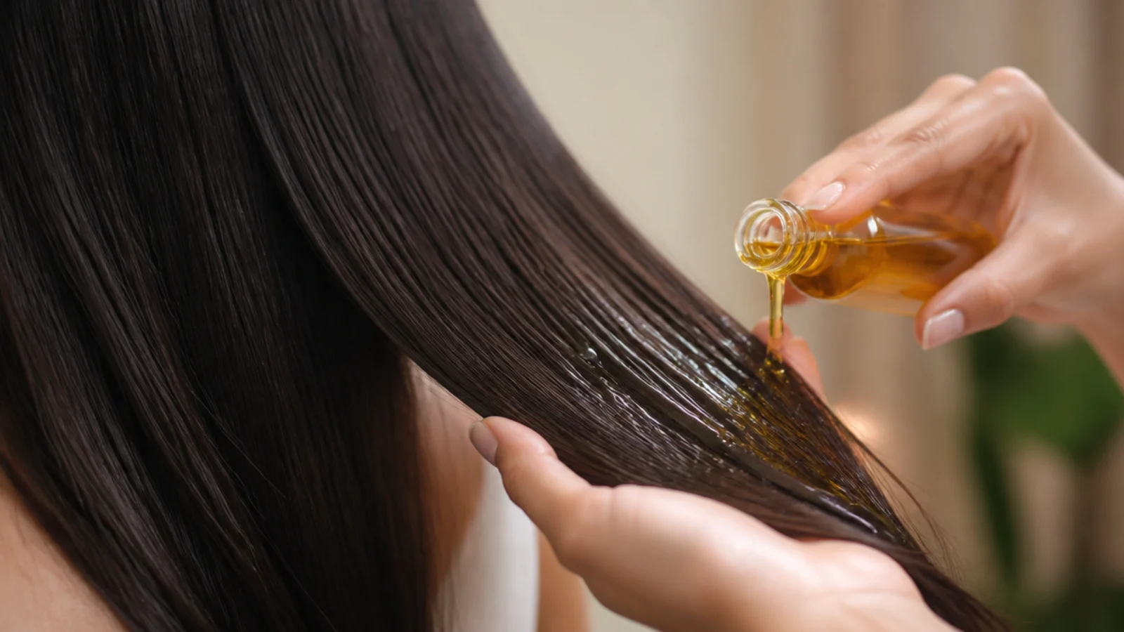 Thick amber castor oil being smoothed onto the ends of long dark hair to seal moisture