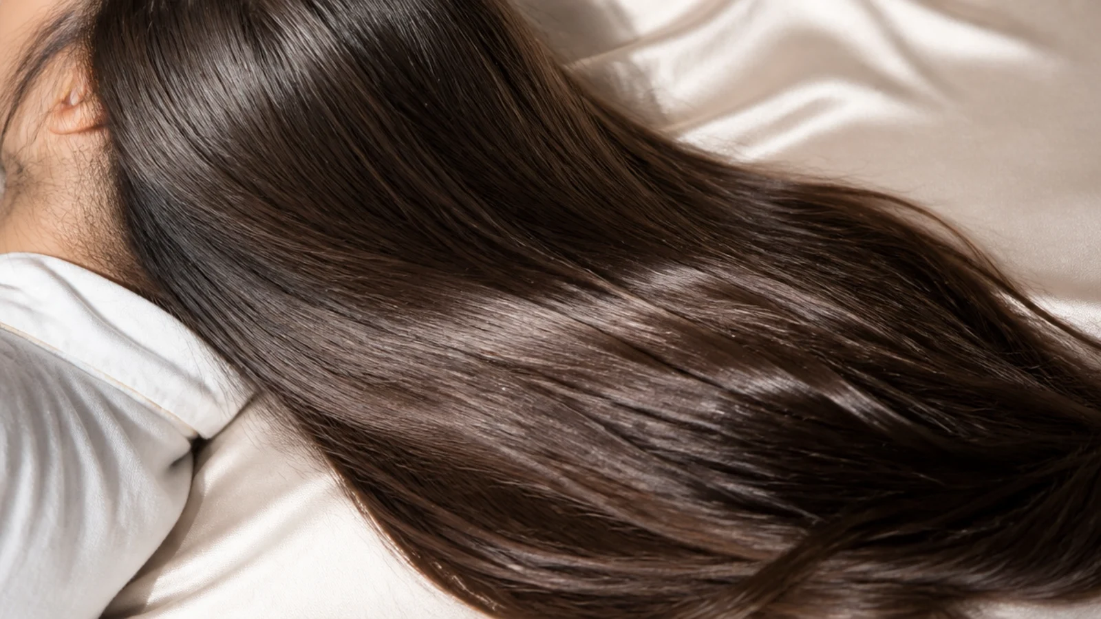 Long hair spread across a champagne satin pillowcase to prevent overnight breakage