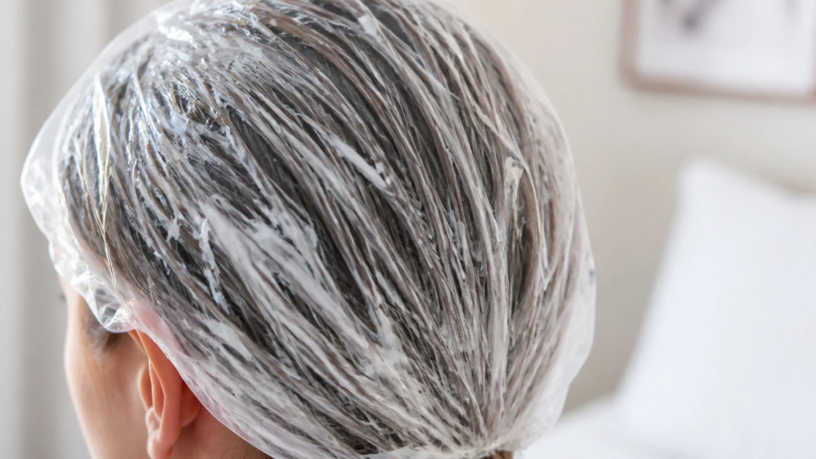 Hair coated in a thick white deep conditioning mask and covered with a clear plastic processing cap