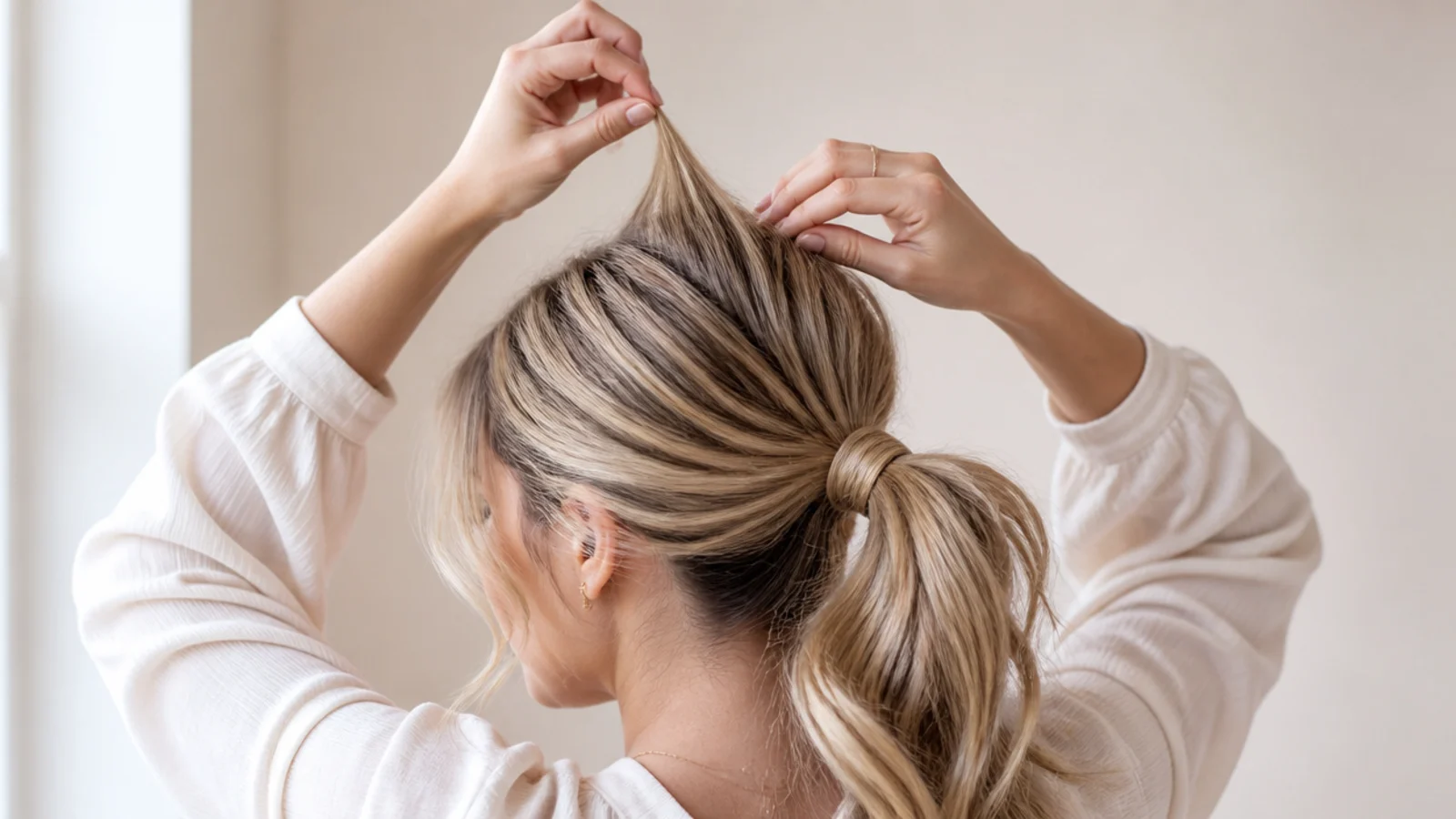 Fingers pinching a small crown section and tugging it upward for volume in a messy ponytail