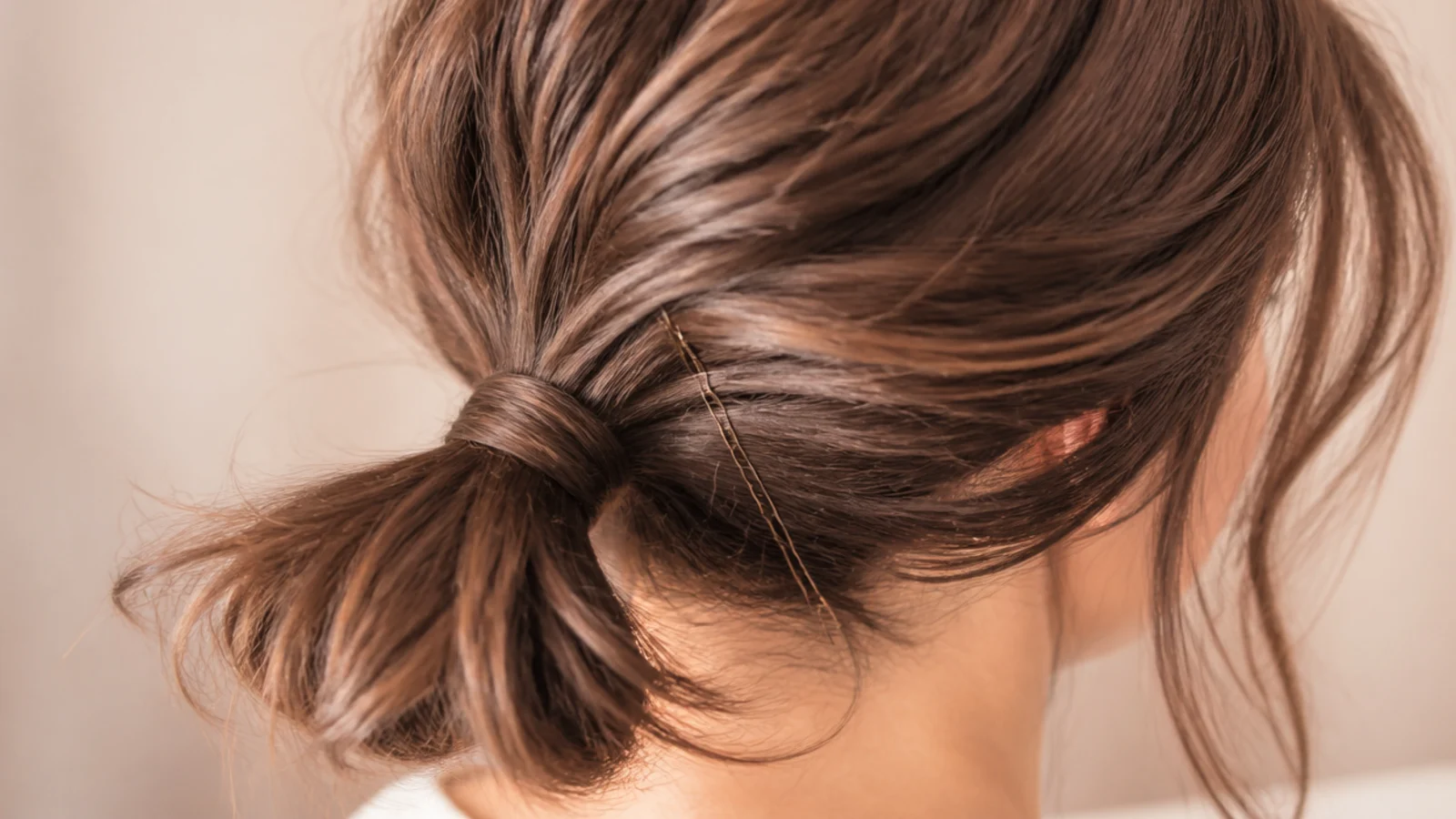 Low messy ponytail on a chin-length bob with pins securing the short layers at the nape