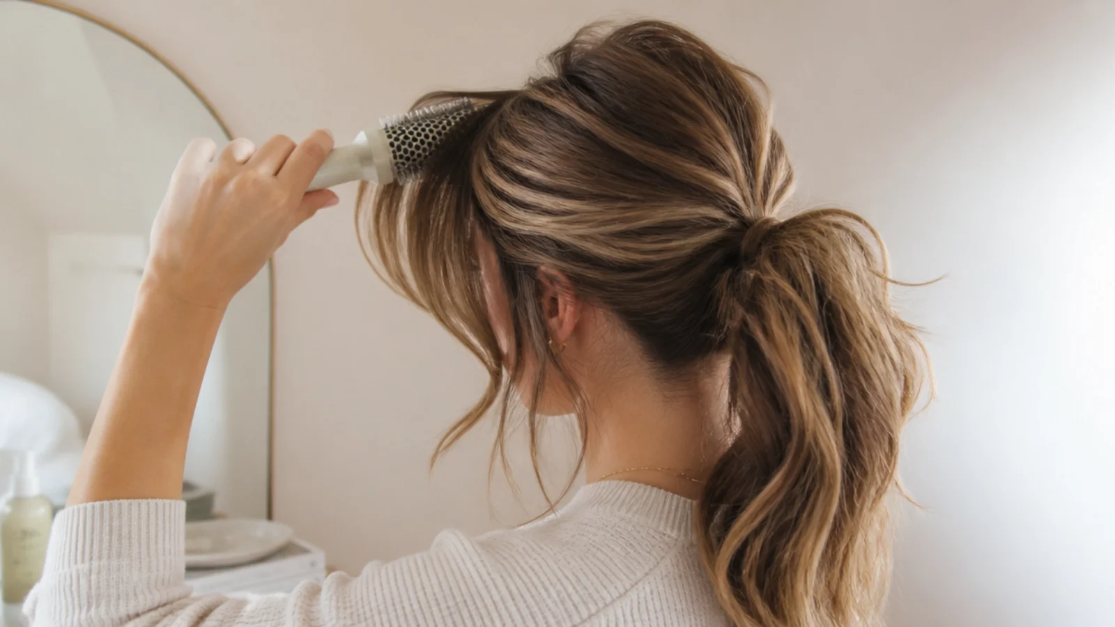 Round brush curving curtain bangs away from the face above a messy ponytail