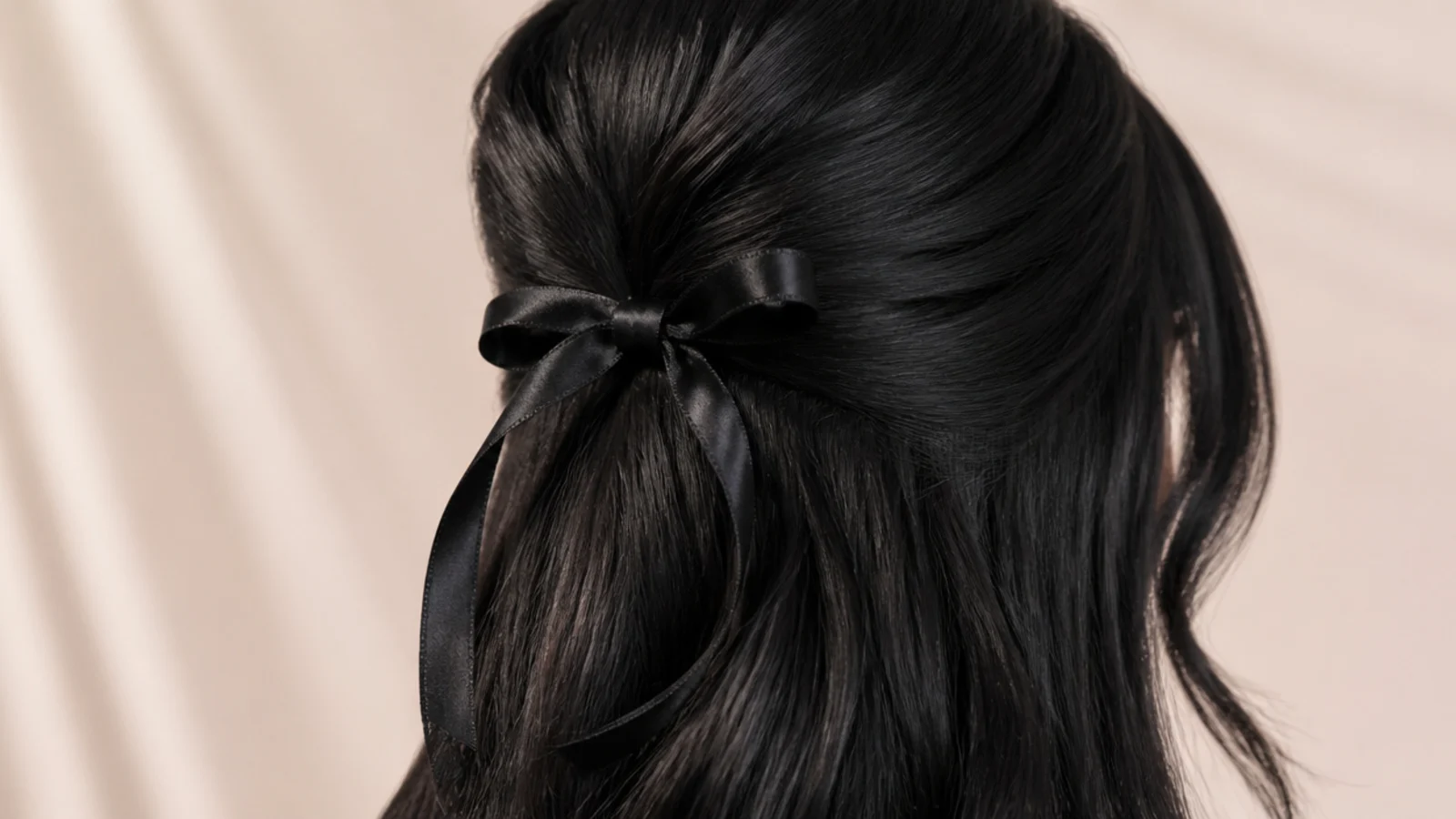 Jet black half-up style secured with a black satin ribbon bow at the back of the head