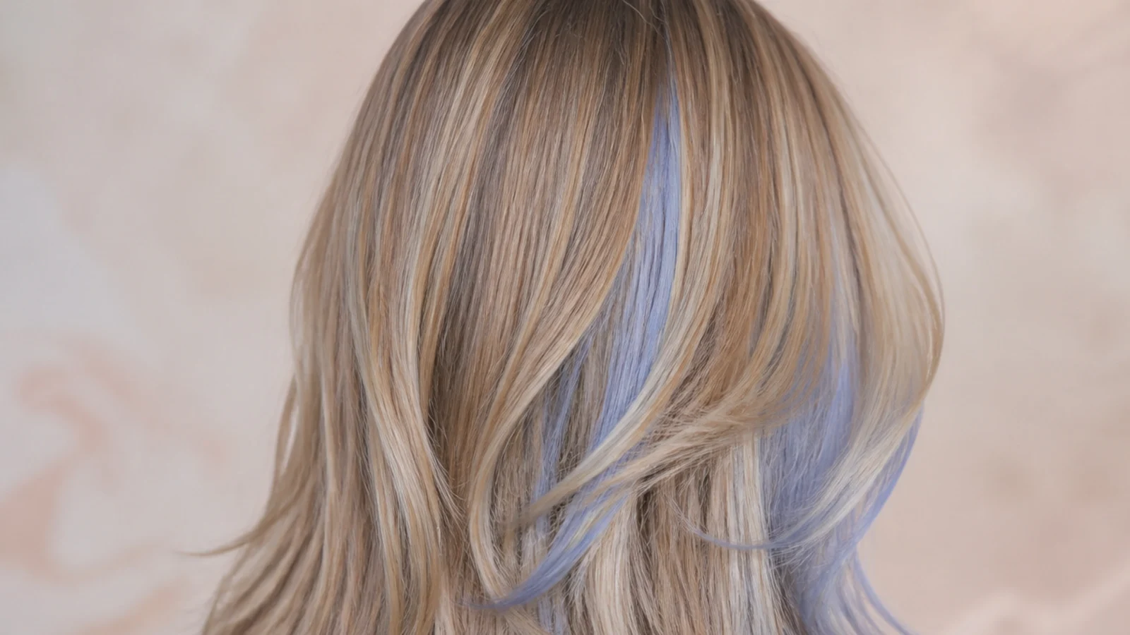 Periwinkle blue money piece brightening the front sections of long blonde hair, viewed from behind
