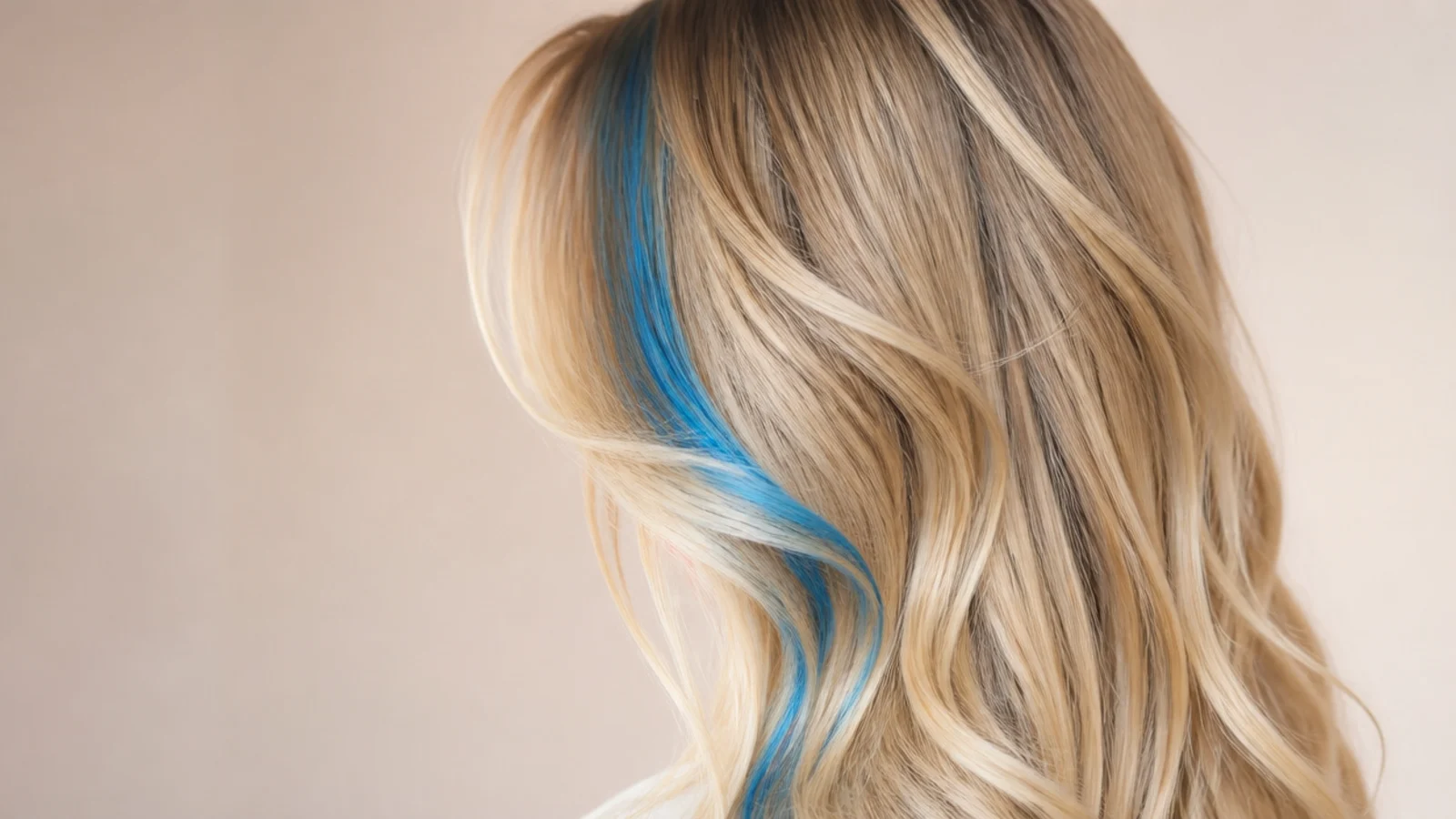 One bright blue streak in the face framing layer of long blonde hair, seen from a three quarter back view