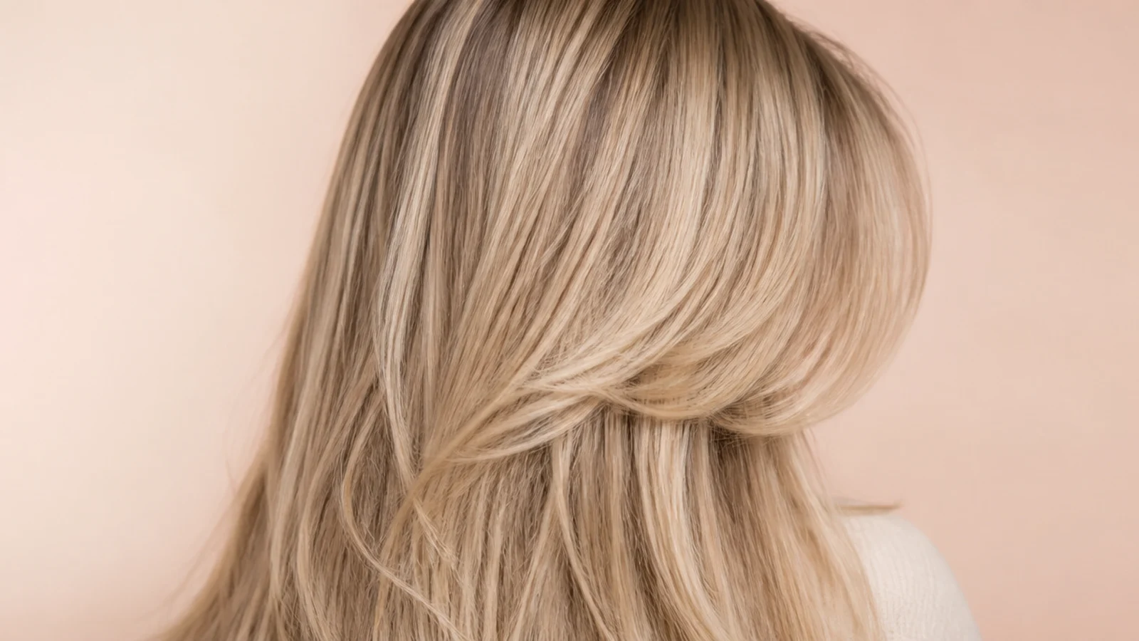 Lash-skimming curtain bangs on long blonde layers, shot from behind with the fringe angling toward the cheekbone