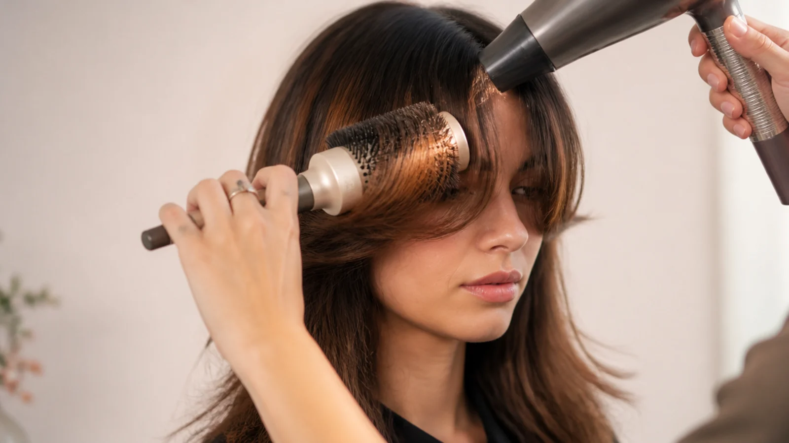 A 2 inch round brush sweeping short curtain bangs away from the face during a blow-dry