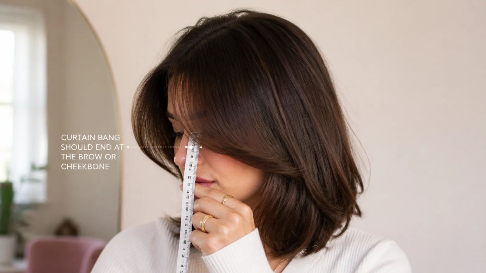 Measuring tape held against a short curtain bang showing the eyebrow length cutting limit