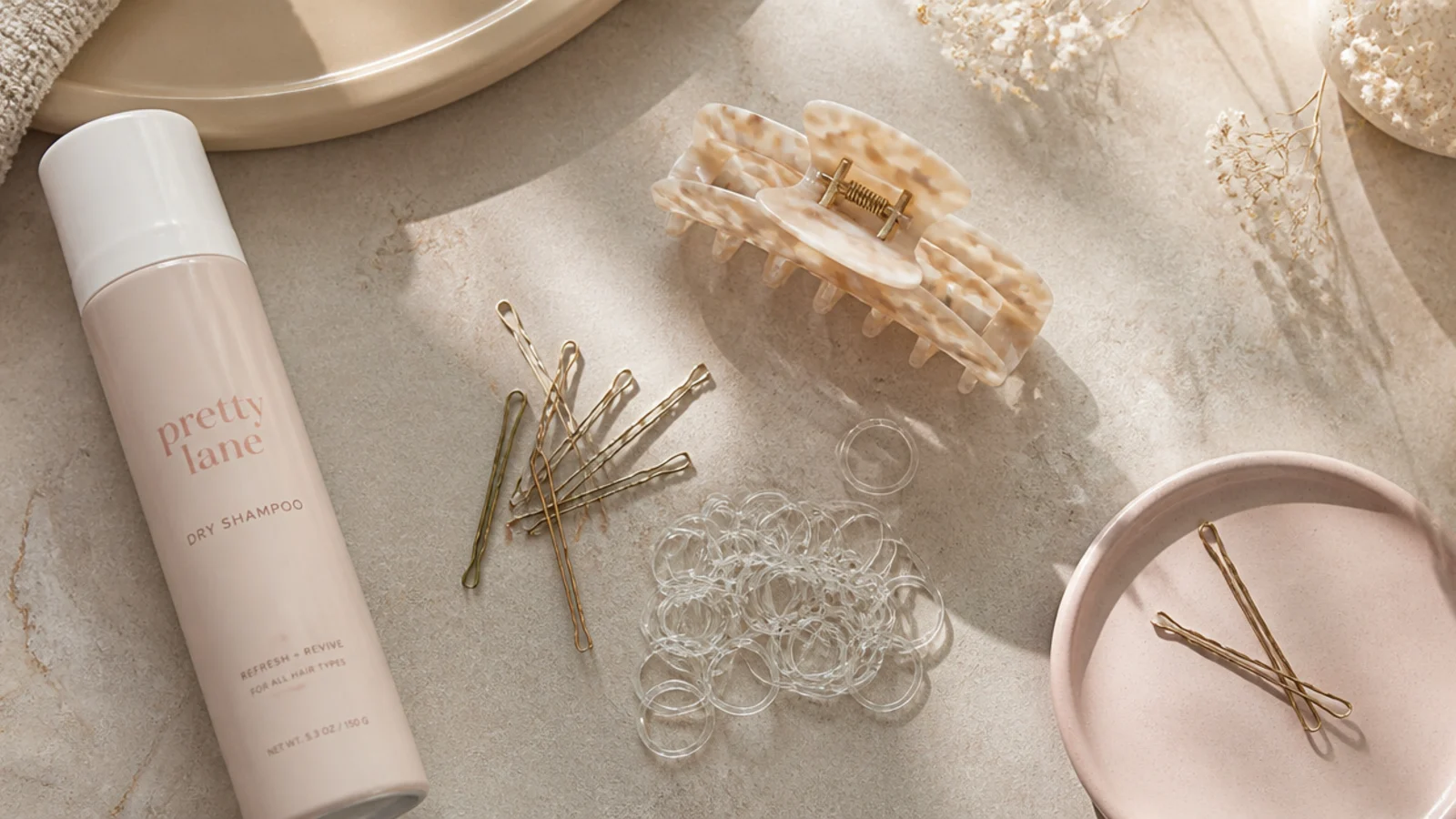 Faceless flat lay of bobby pins, clear elastics, a claw clip and dry shampoo for no-heat styling