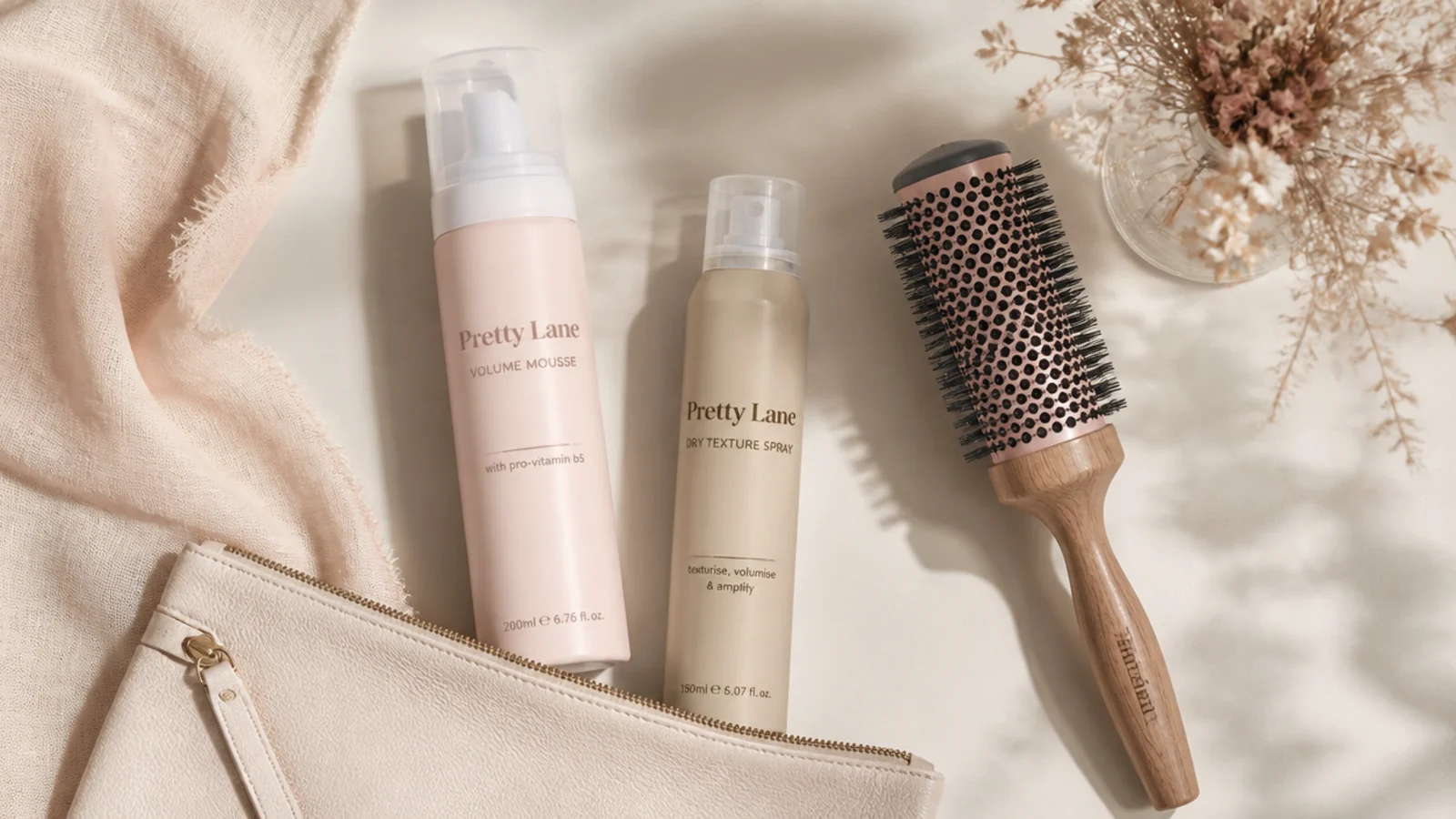 Faceless flat lay of lightweight volume products for fine hair including mousse, dry texture spray and a round brush