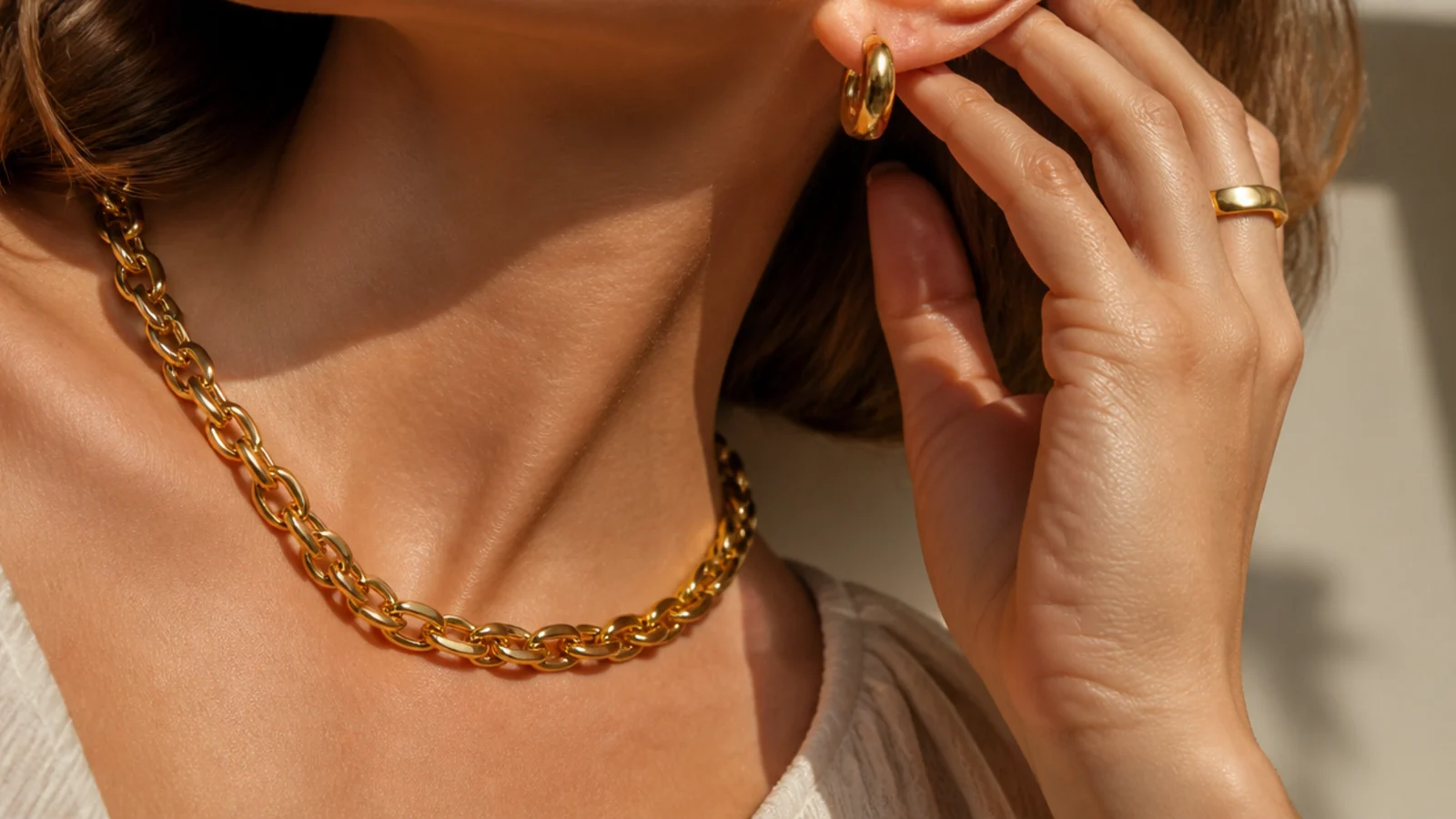 Faceless close-up of a chunky gold chain necklace and huggie hoops marked for water-resistant daily wear