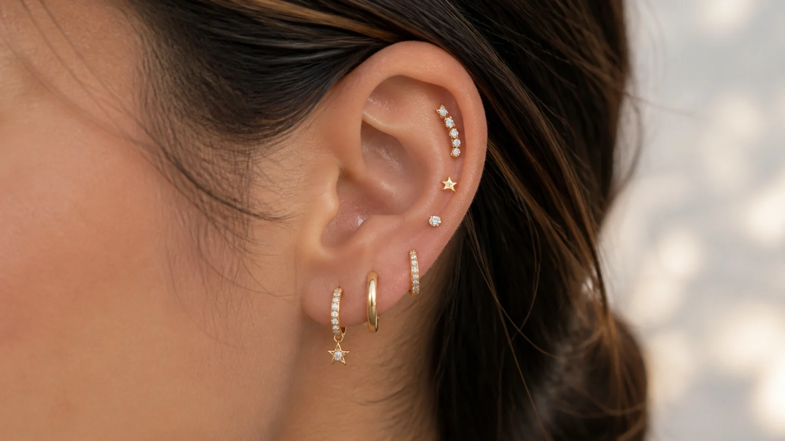 Faceless close-up of a curated ear stack with huggies, studs and a climber on a single ear