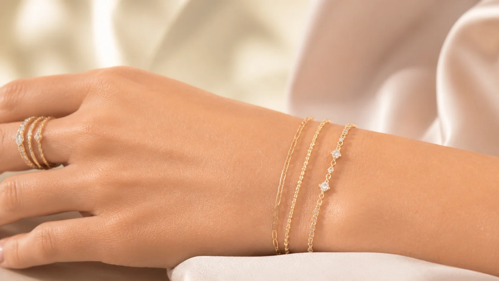 Faceless close-up of thin stackable rings and dainty chain bracelets layered on a wrist