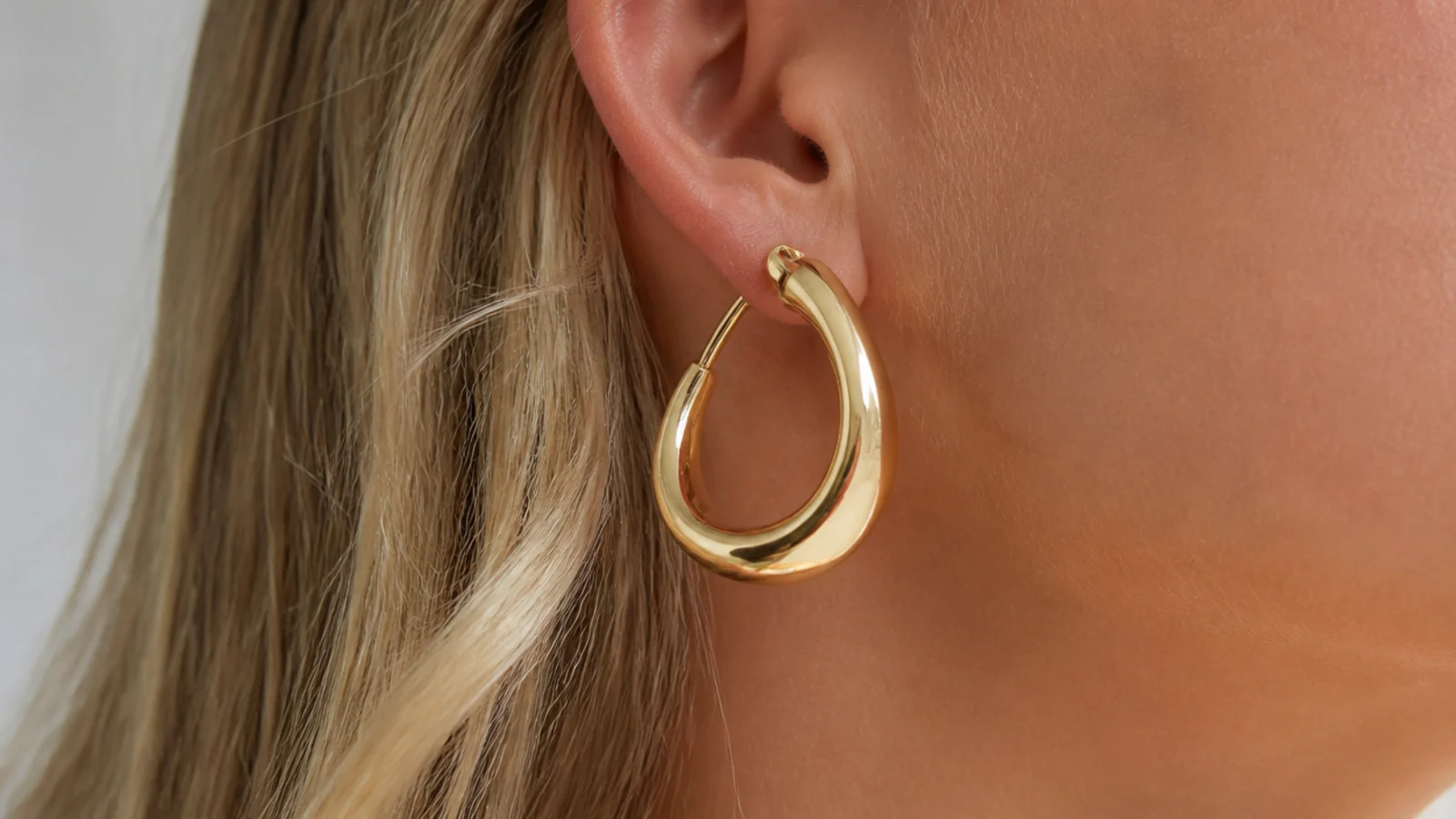 Faceless close-up of oversized sculptural gold hoops with a smooth architectural shape