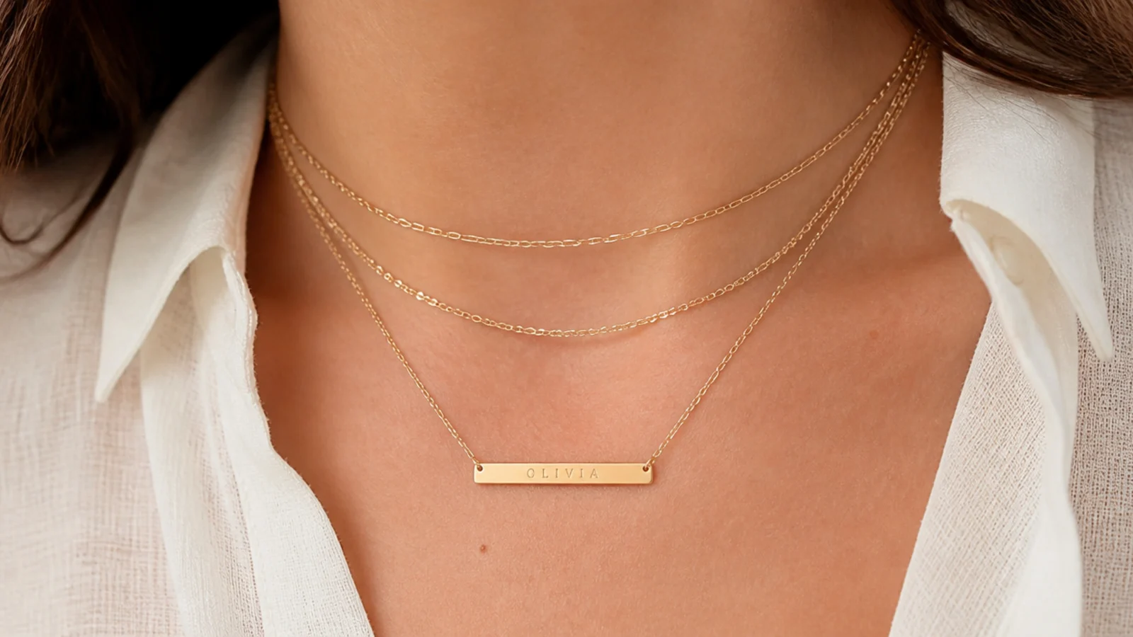 Faceless close-up of thin gold-filled chains and a personalized bar necklace for daily wear
