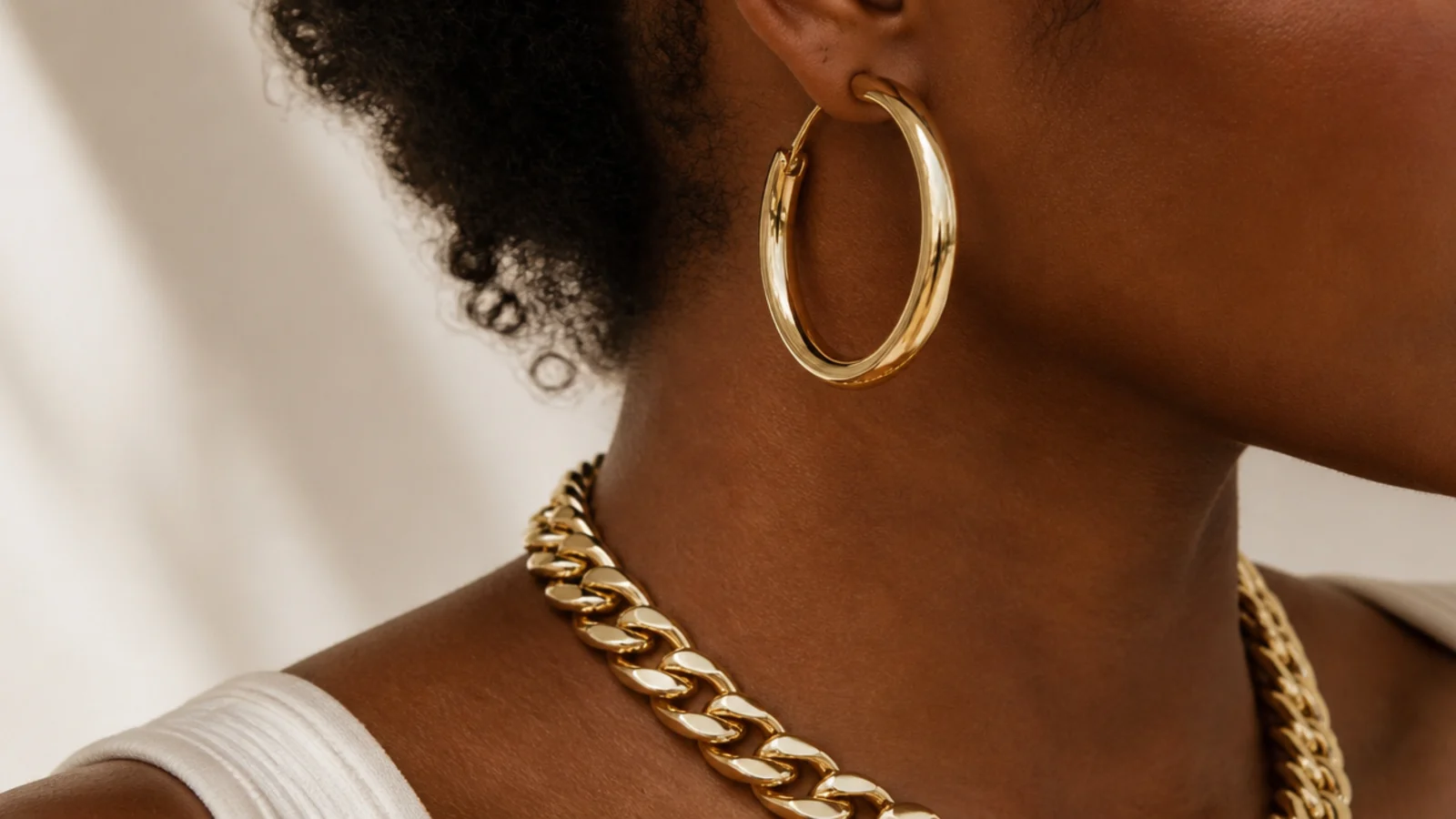 Faceless close-up of bold gold hoops and a thick chain designed to flatter deeper skin tones