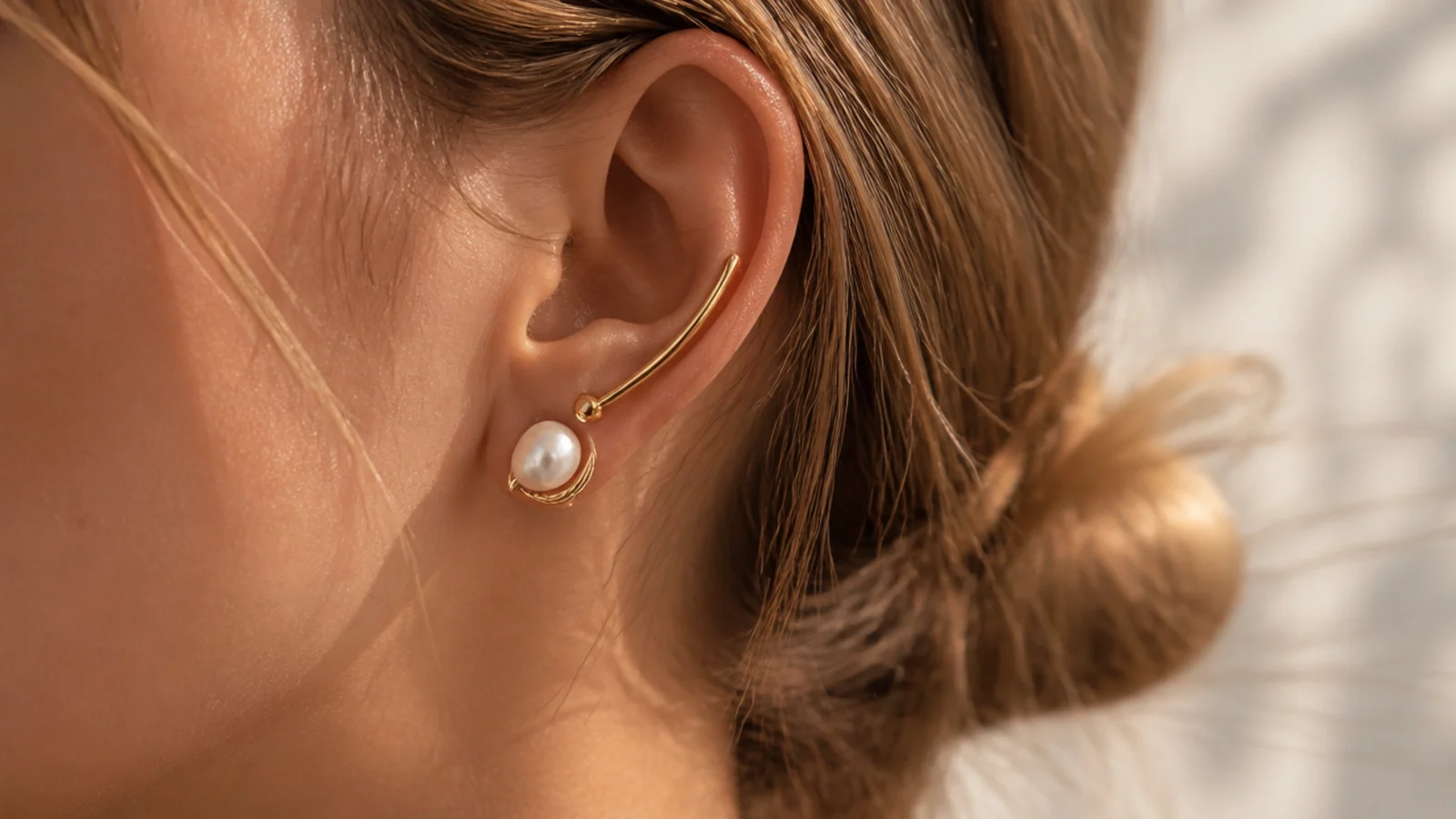 Faceless close-up of an asymmetric freshwater pearl and gold ear piece with a delicate curved design