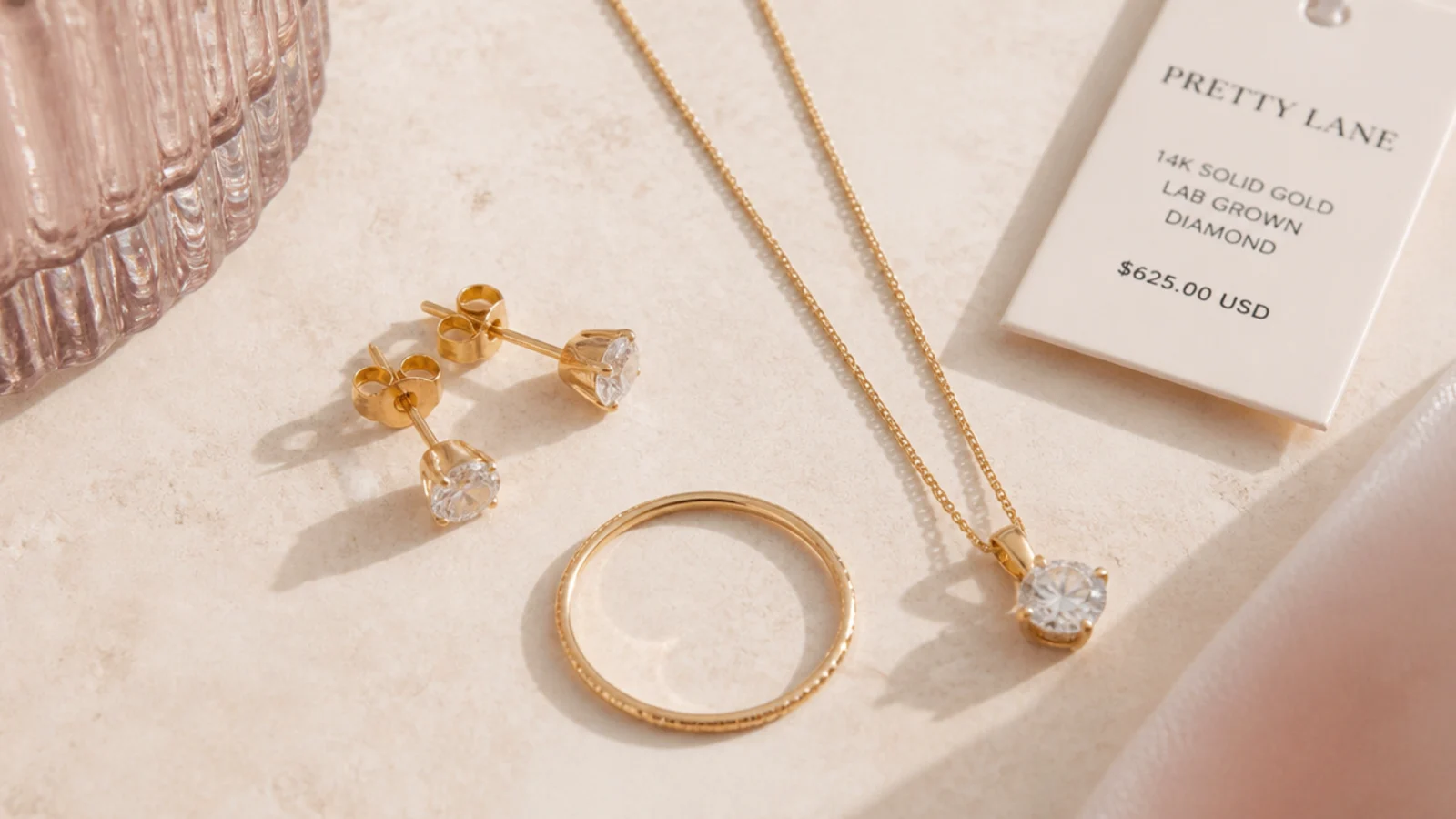 Faceless flat-lay of solid gold studs, a thin stacking ring and a lab-grown pendant under a value tag