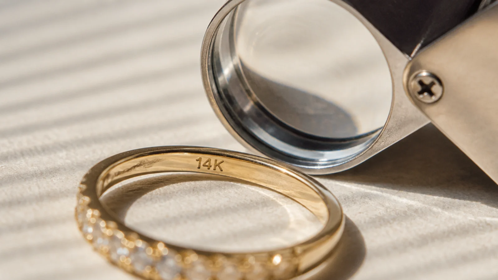 Faceless close-up of a gold ring inner band stamped 14K next to a jeweler's loupe