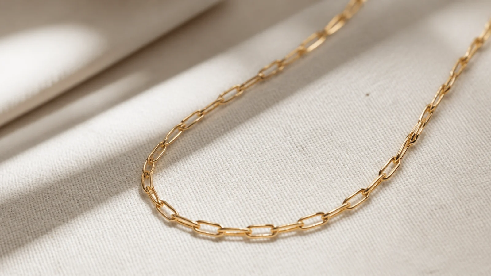 Faceless close-up of a gold chain photographed at a 45-degree angle in natural window light
