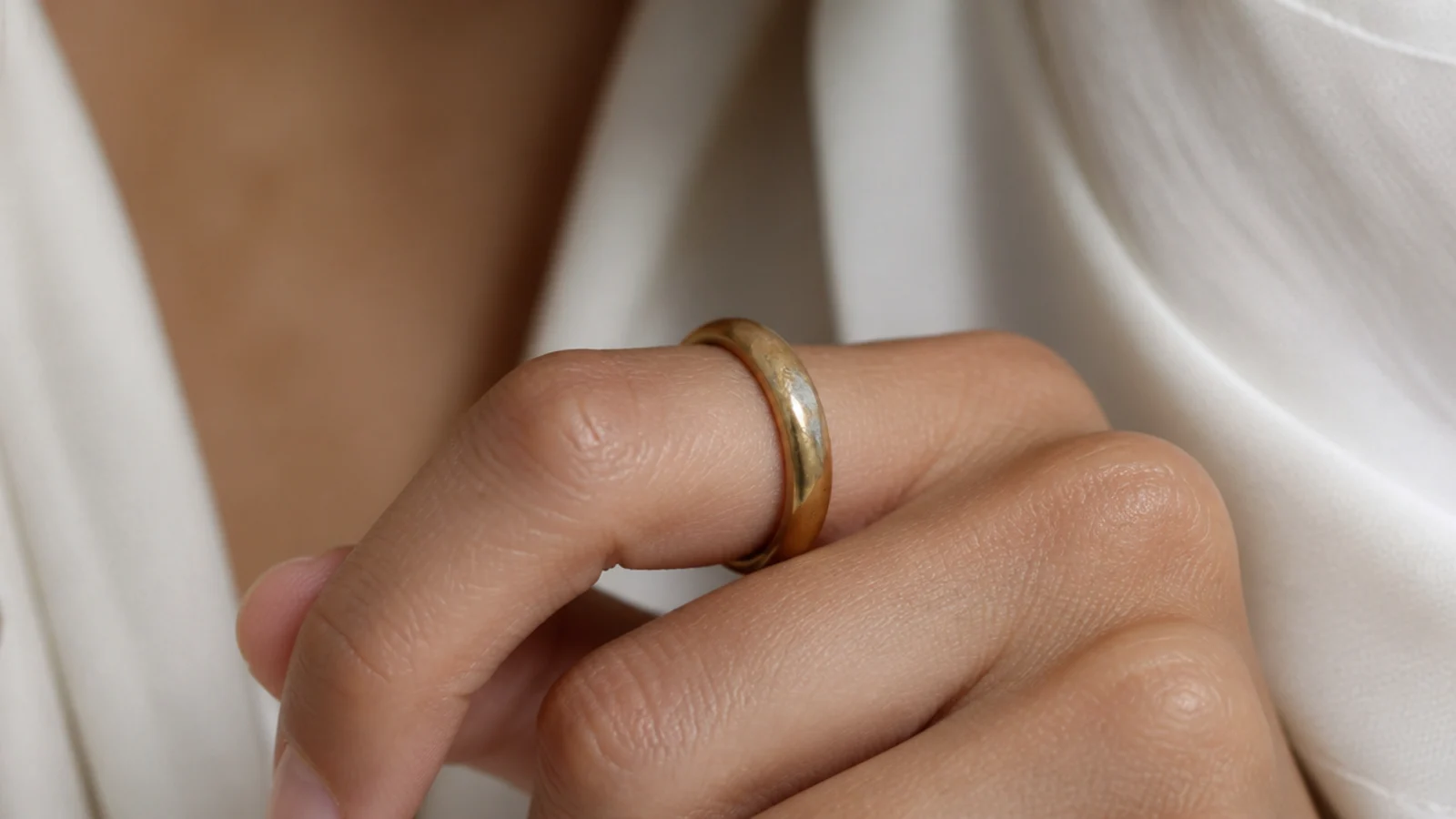 Faceless close-up of a worn gold-plated ring showing the base metal exposed at the band edge
