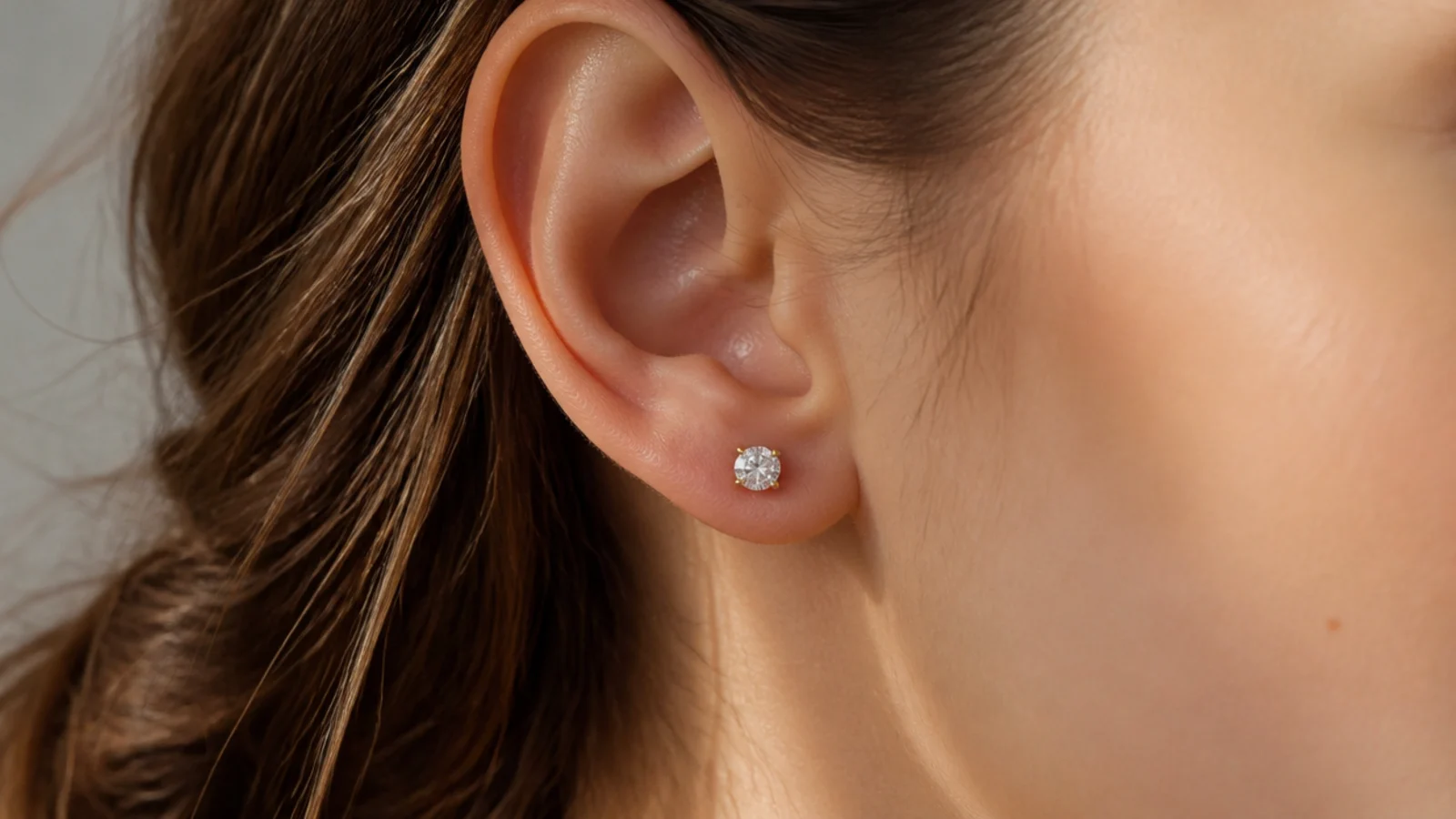 Faceless close-up of a small round diamond stud earring in a four-prong gold setting